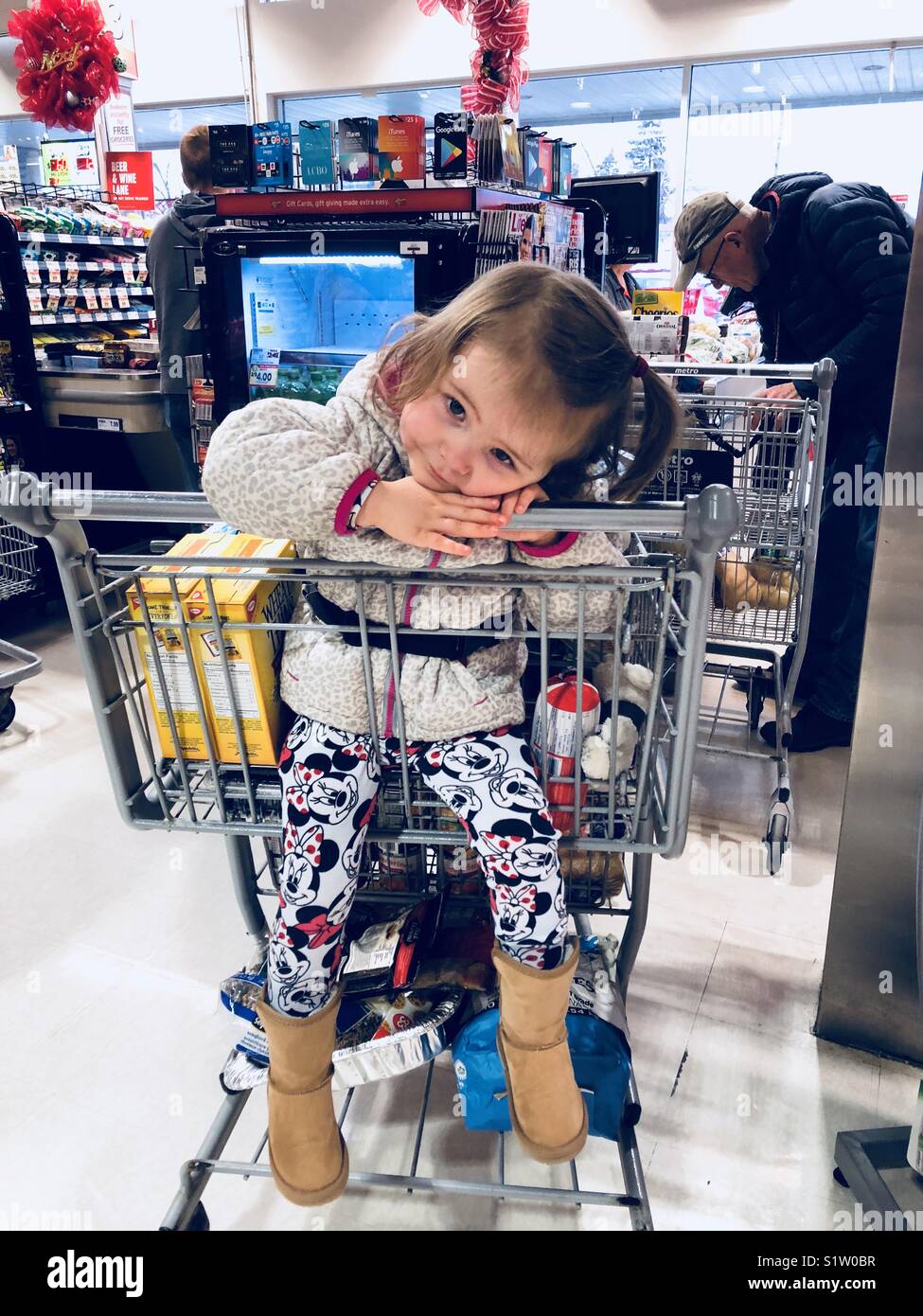 Waiting in line at the grocery store with a toddler girl resting her head in the cart and a man ahead in line with the cashier - Smartphone Captured Stock Image