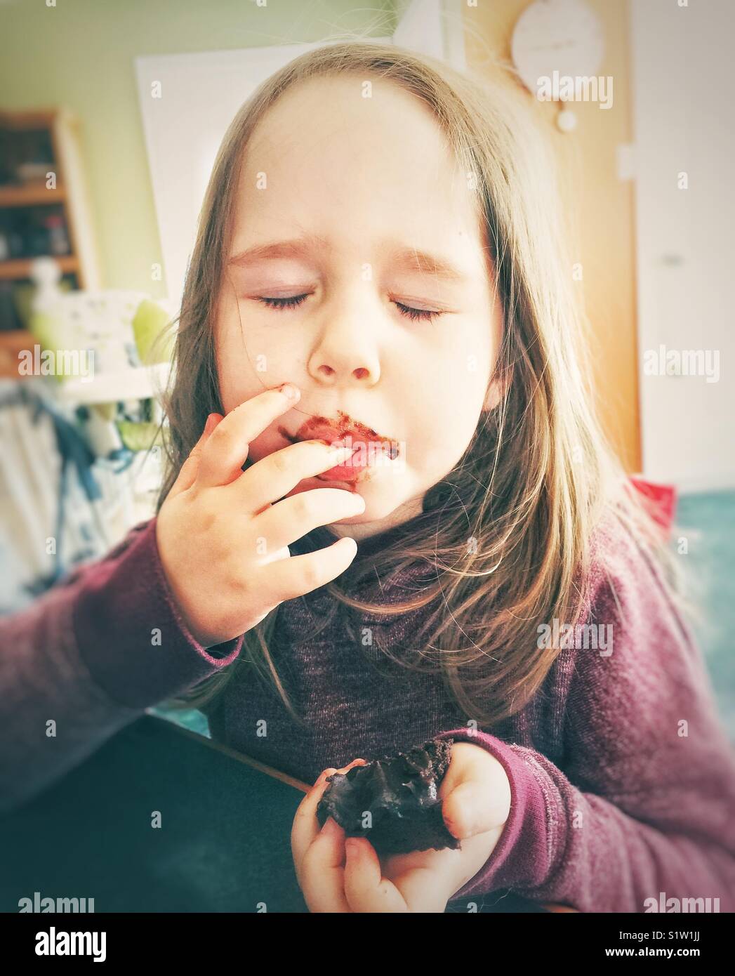4 year old girl eating a chocolate brownie with a look of pure enjoyment on her face Stock Photo