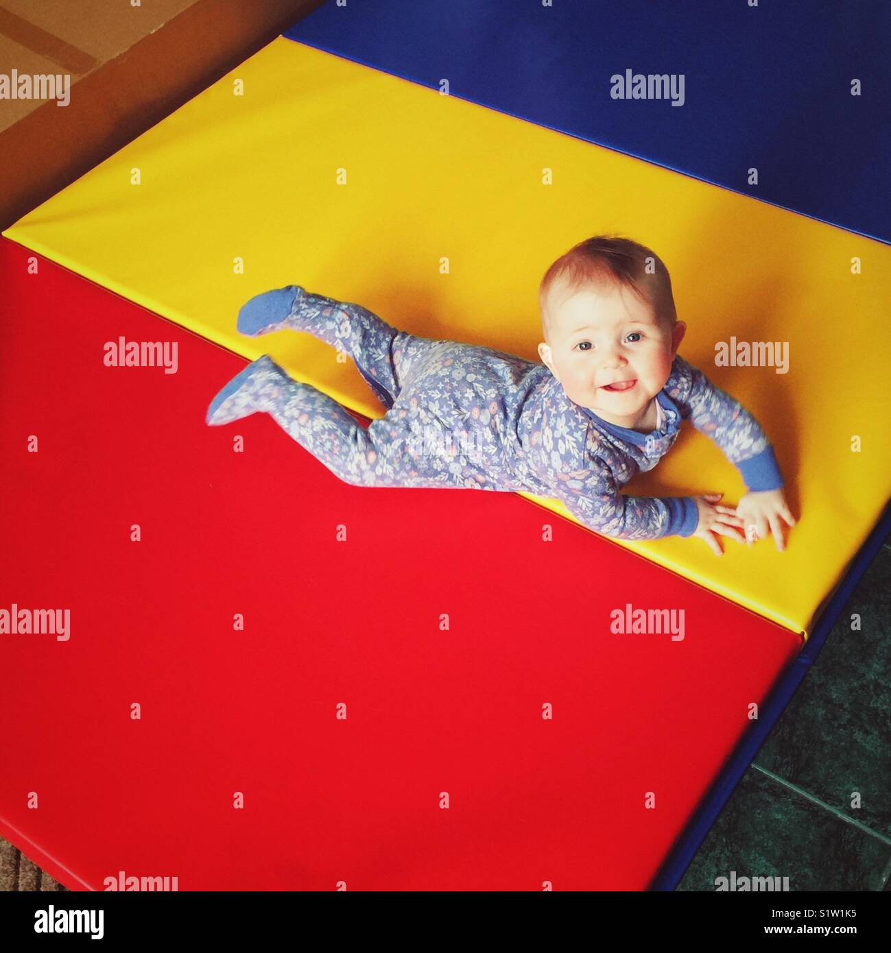 Baby girl crawling on high density multi-coloured gym mat Stock Photo