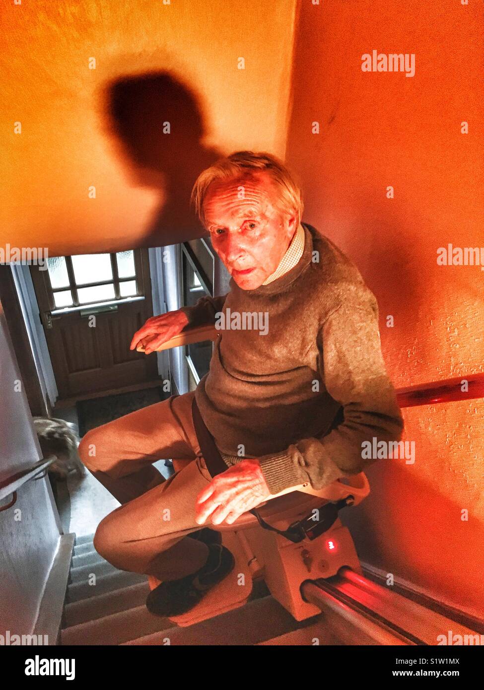 Elderly man using a stair lift to go upstairs in his home. - Smartphone Captured Stock Image