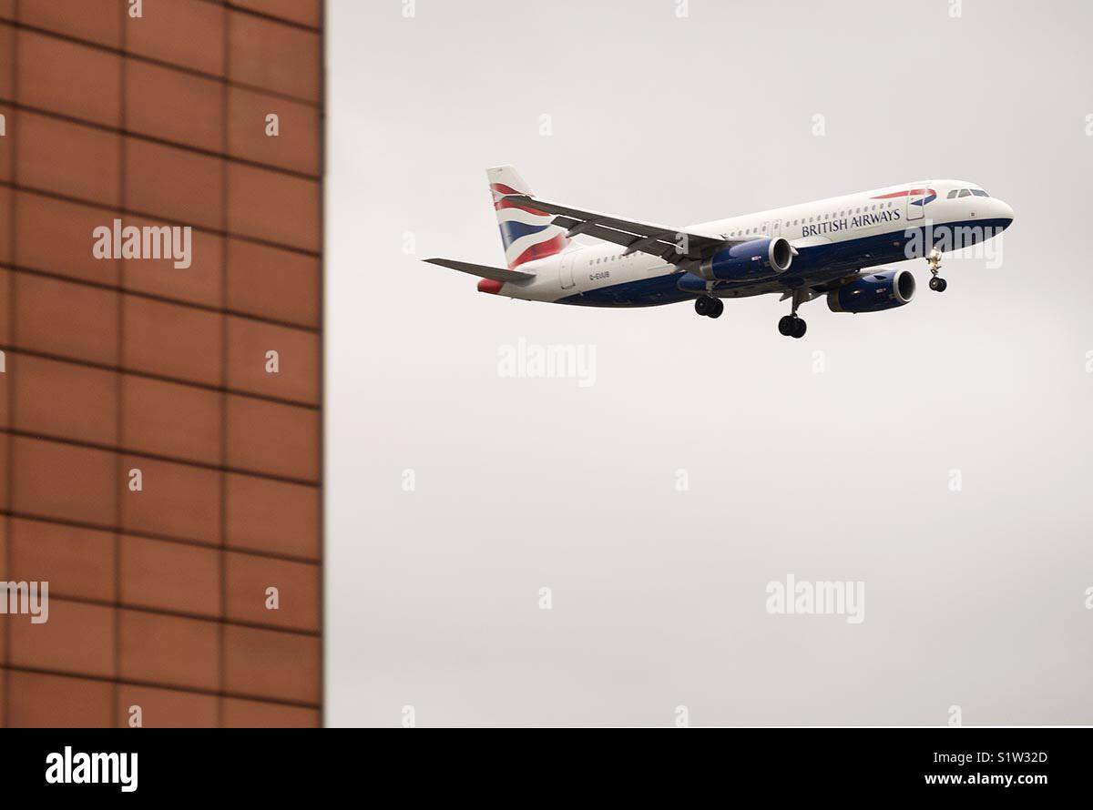 A British Airways aircraft comes in to land at Heathrow Airport London past a red tiled wall - Smartphone Captured Stock Image