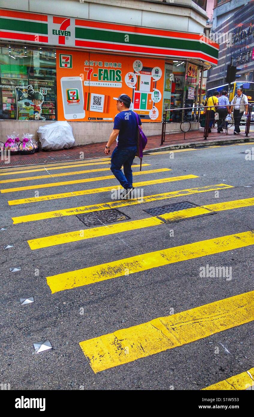 A man crosses the road by a 7 eleven shop in Hong Kong - Smartphone Captured Stock Image