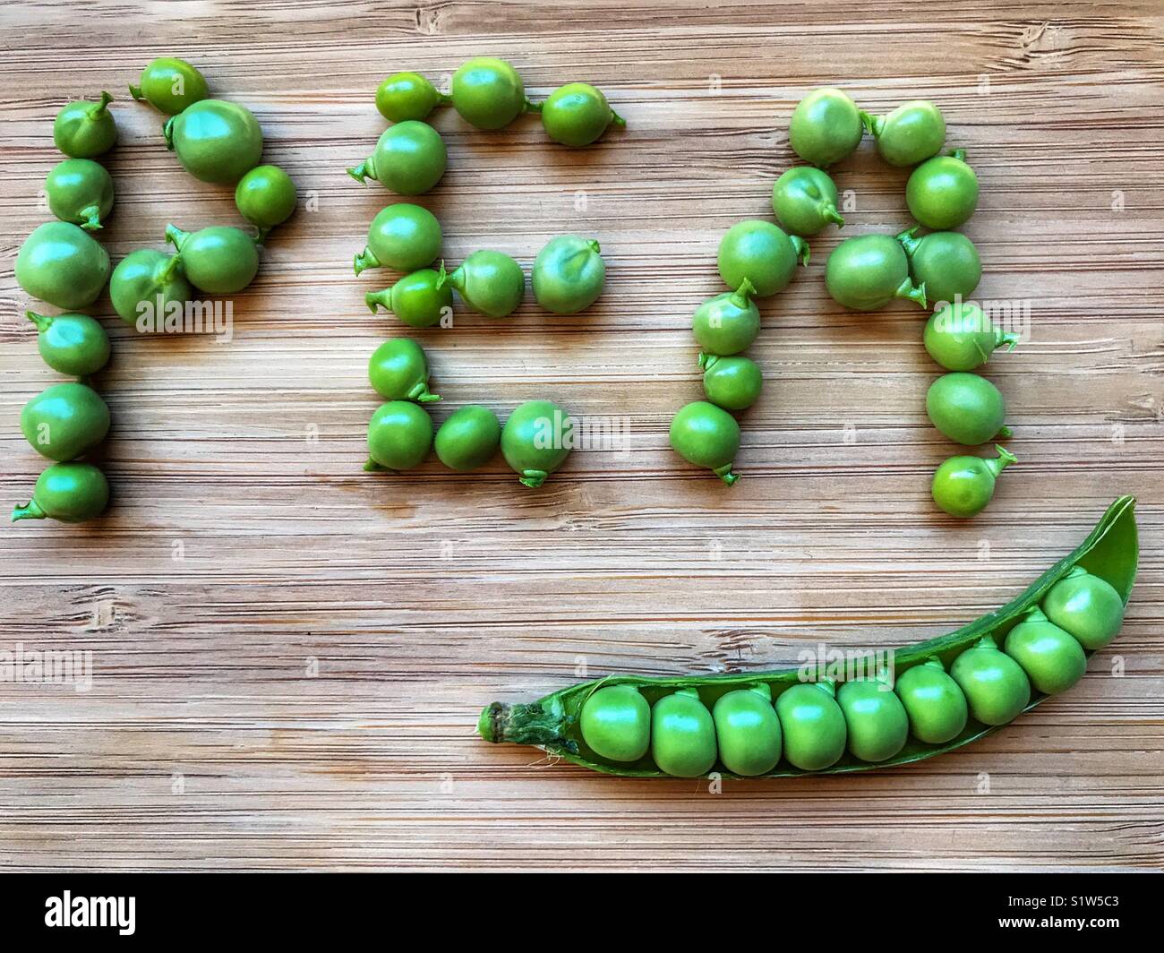Fresh green peas in a pod, and peas spelling out the word pea, on a bamboo board with copy space - Smartphone Captured Stock Image