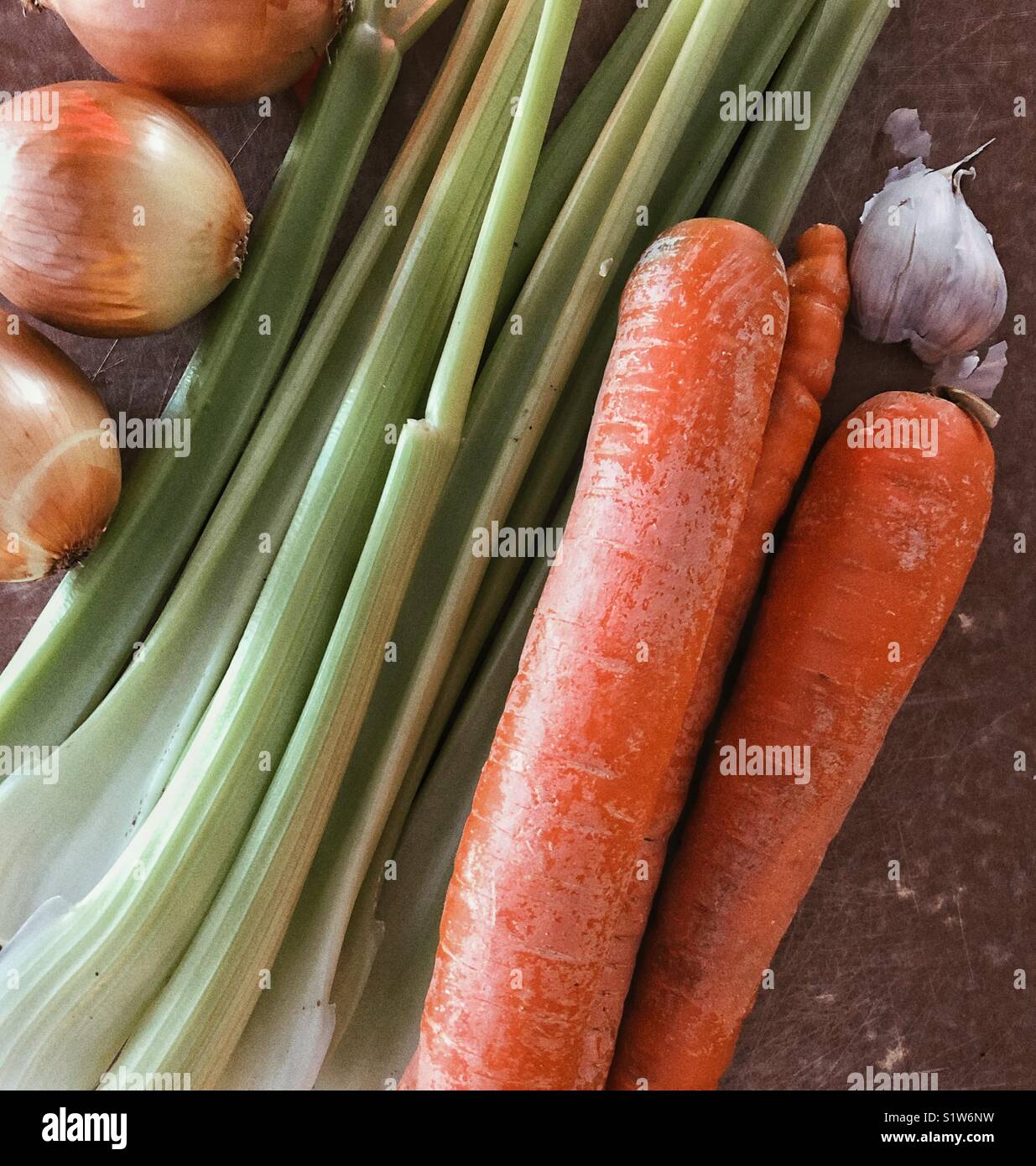 Fresh vegetables consisting of onions, celery, carrots and garlic on a brown cutting board - Smartphone Captured Stock Image