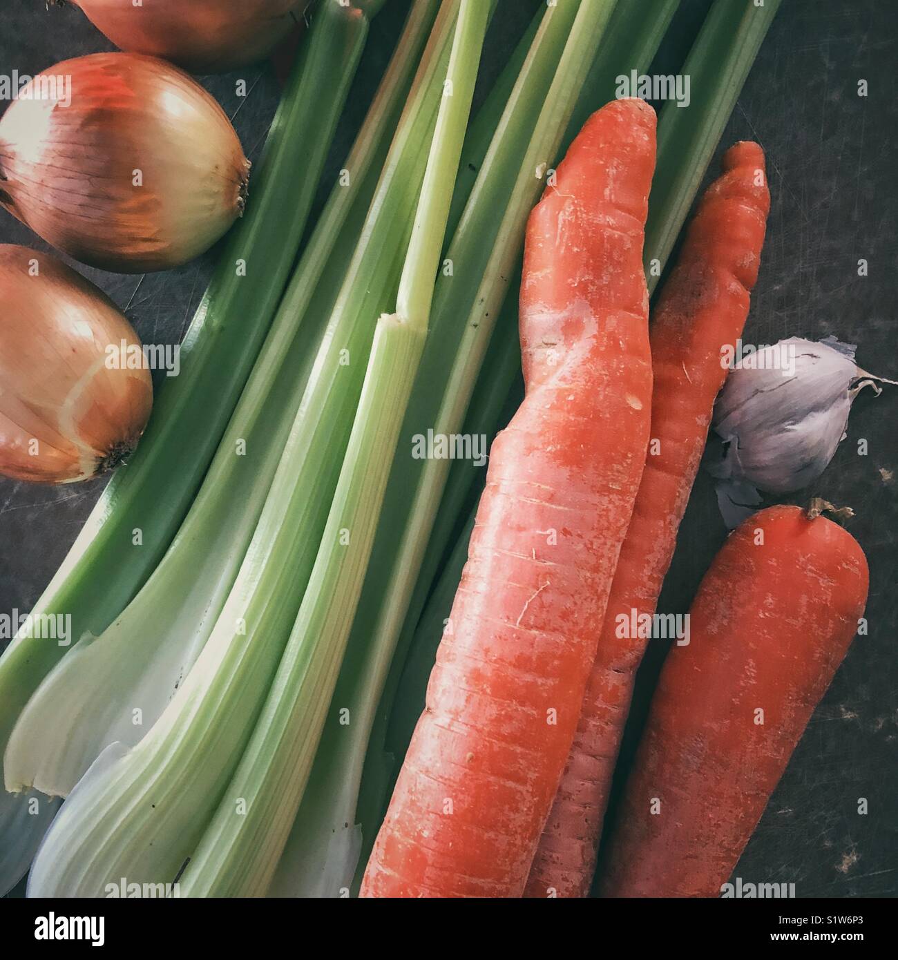 Fresh onions, celery stalks, large carrots, and garlic bulb on a brown cutting board Stock Photo