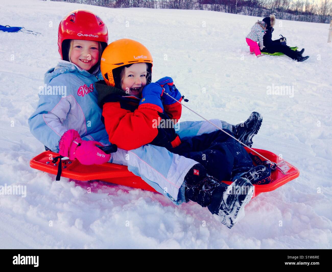 Girls / kids / children / child sledging on a sledge / sled on new snow. Stock Photo