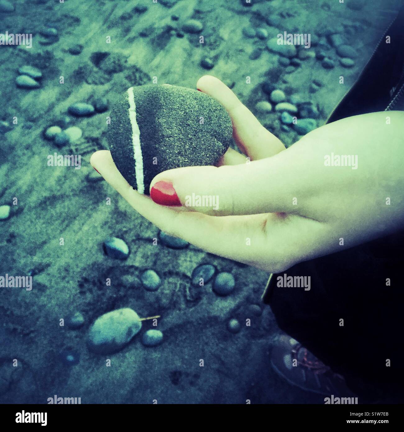 Hand with red nail polish holding rock on a beach Stock Photo