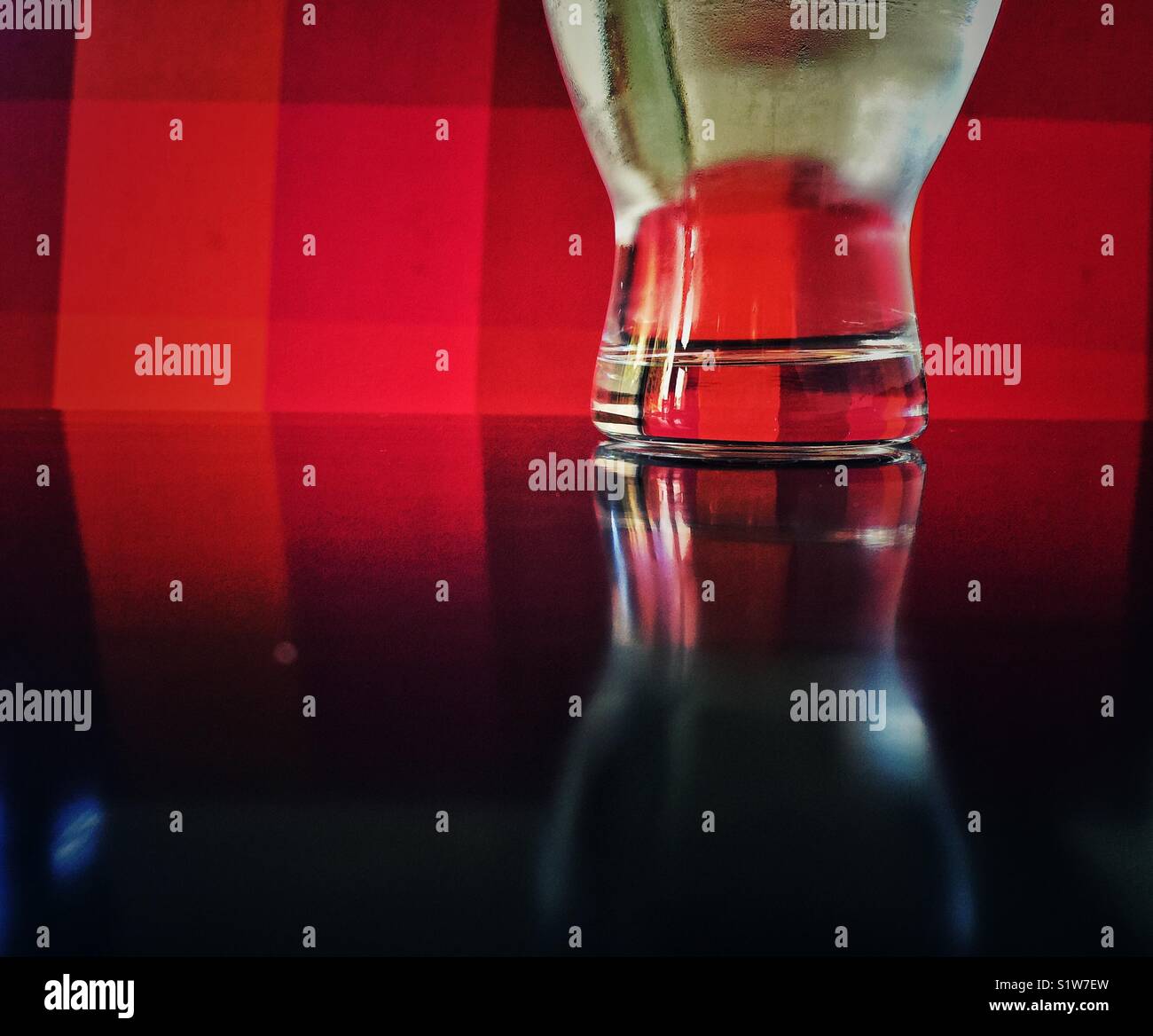 Glass full of water reflects  on a wooden table against red background - Smartphone Captured Stock Image
