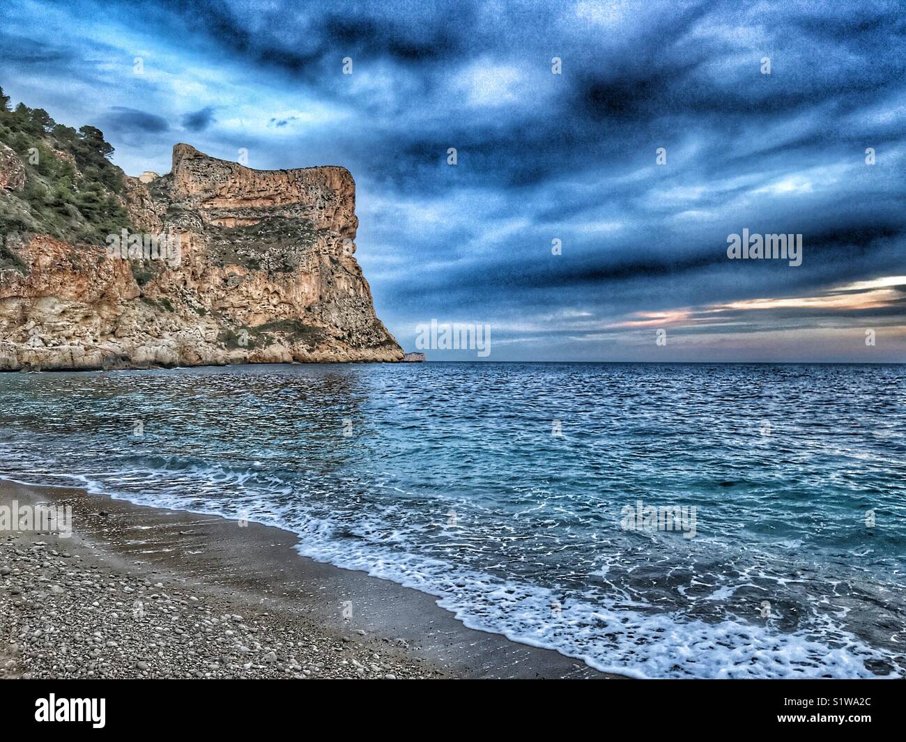 Pebble beach to headland cliff, late afternoon, Cala Moraig, Javea, Alicante, Spain - Smartphone Captured Stock Image