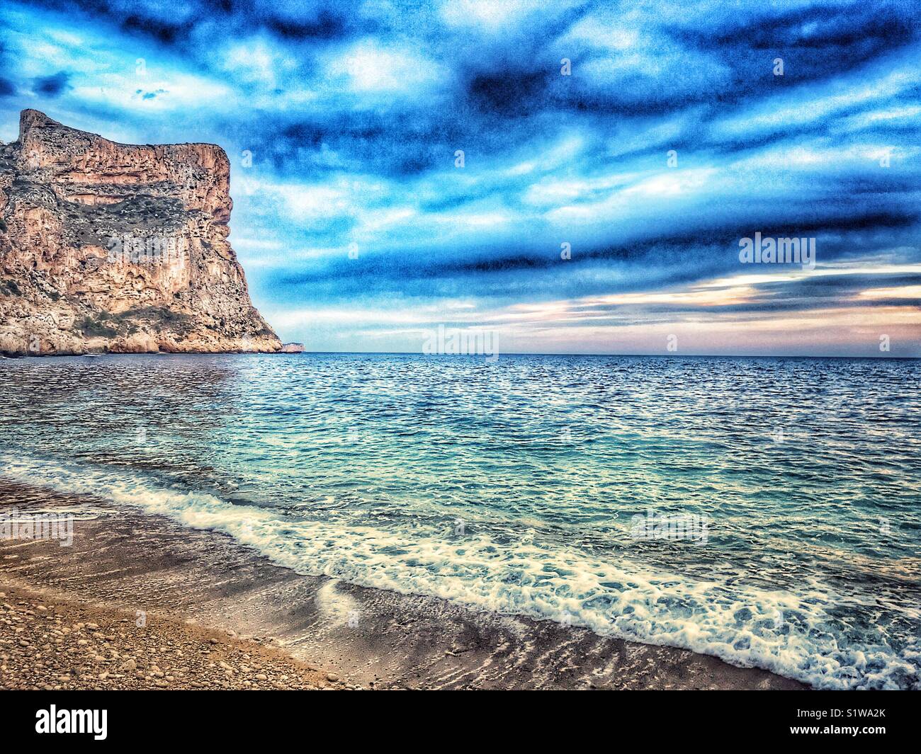 Pebble beach to headland cliff, late afternoon, Cala Moraig, Javea, Alicante, Spain - Smartphone Captured Stock Image