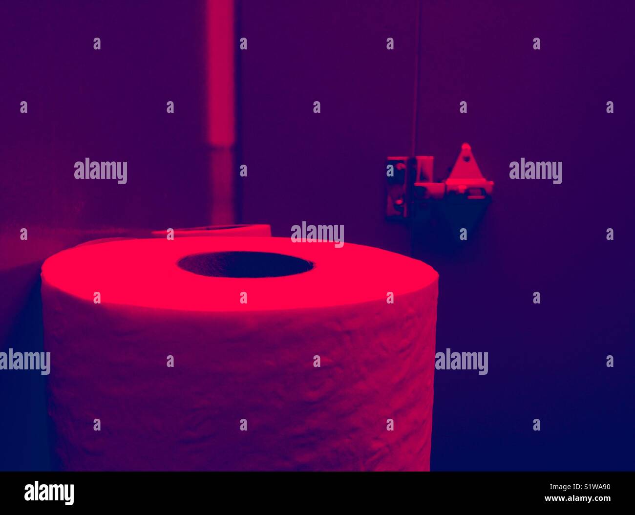 Red tinted photo of toilet paper roll in public restroom Stock Photo