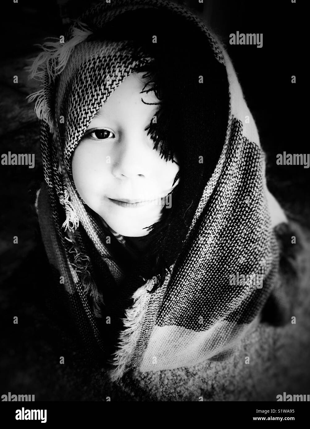 Portrait of a girl wrapped in blanket covering head and eye in black and white Stock Photo