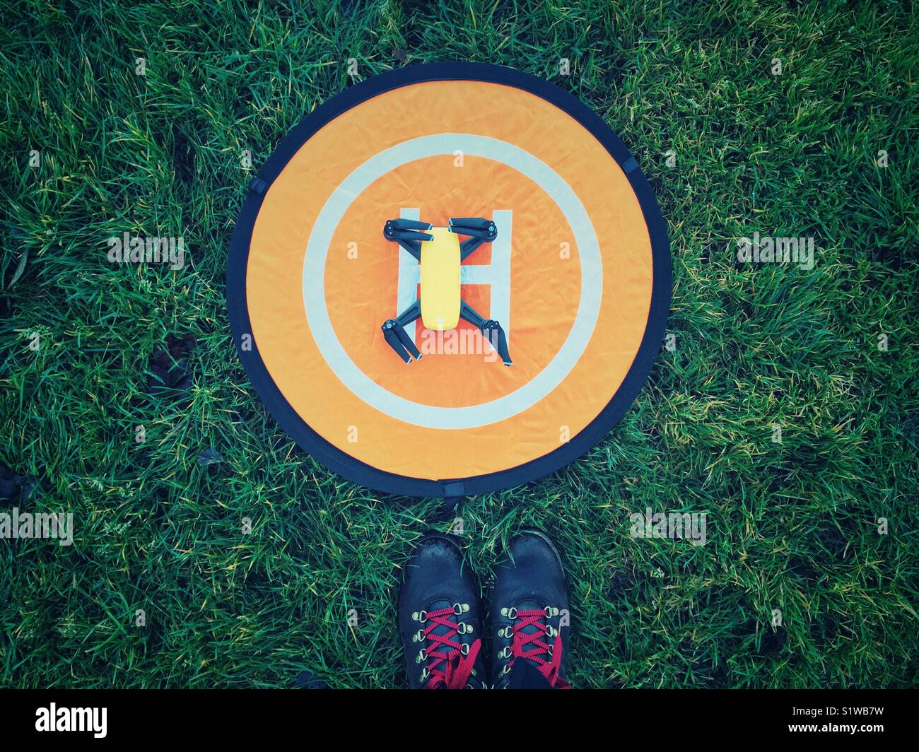 Spark drone on home landing pad on the grass with feet in hiking boots - Smartphone Captured Stock Image