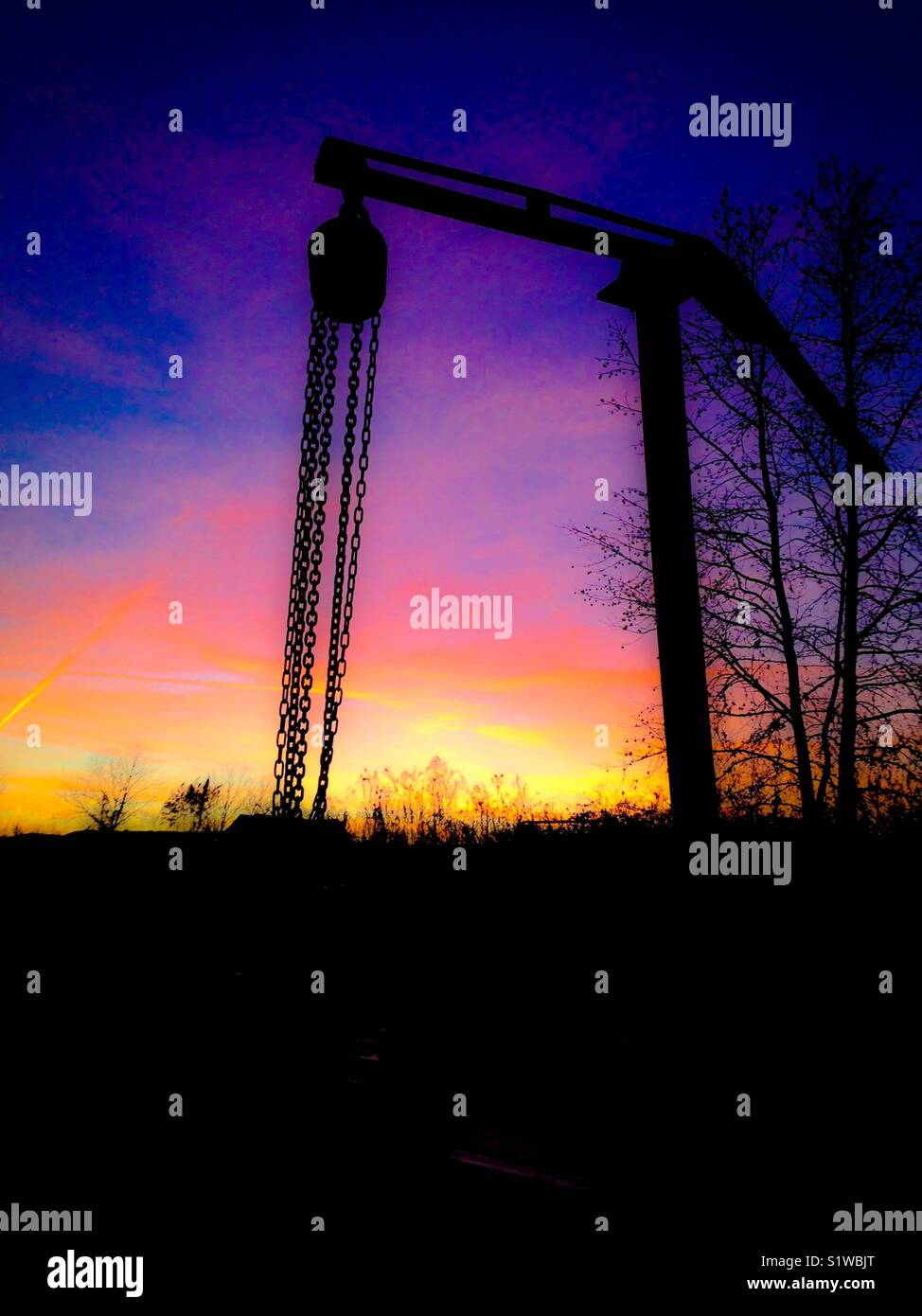 Brightly colored sunset with log lifting rig in silhouette on North Carolina farm - Smartphone Captured Stock Image