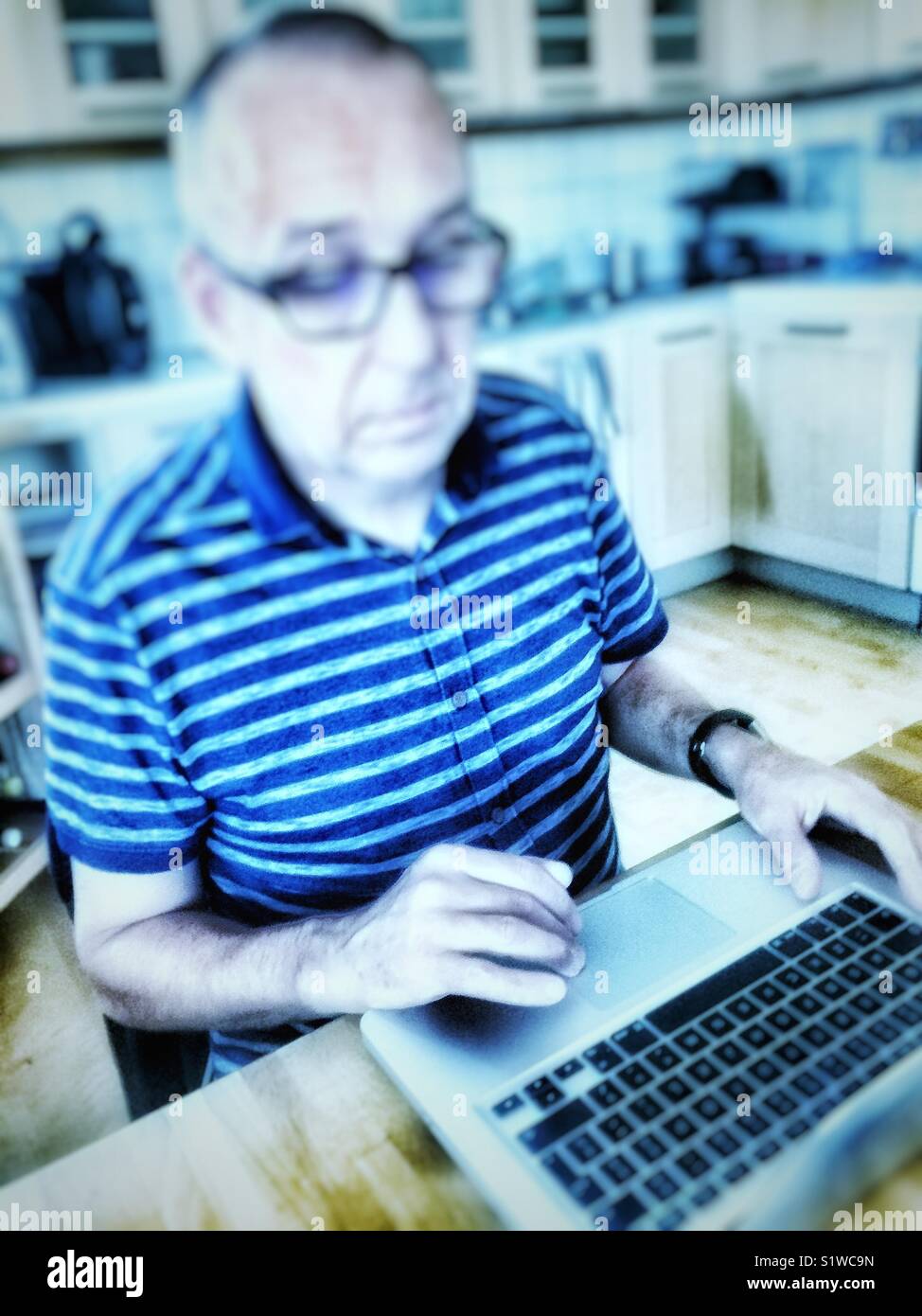 Unhappy serious middle aged man working on laptop in kitchen at home, Sweden - Smartphone Captured Stock Image