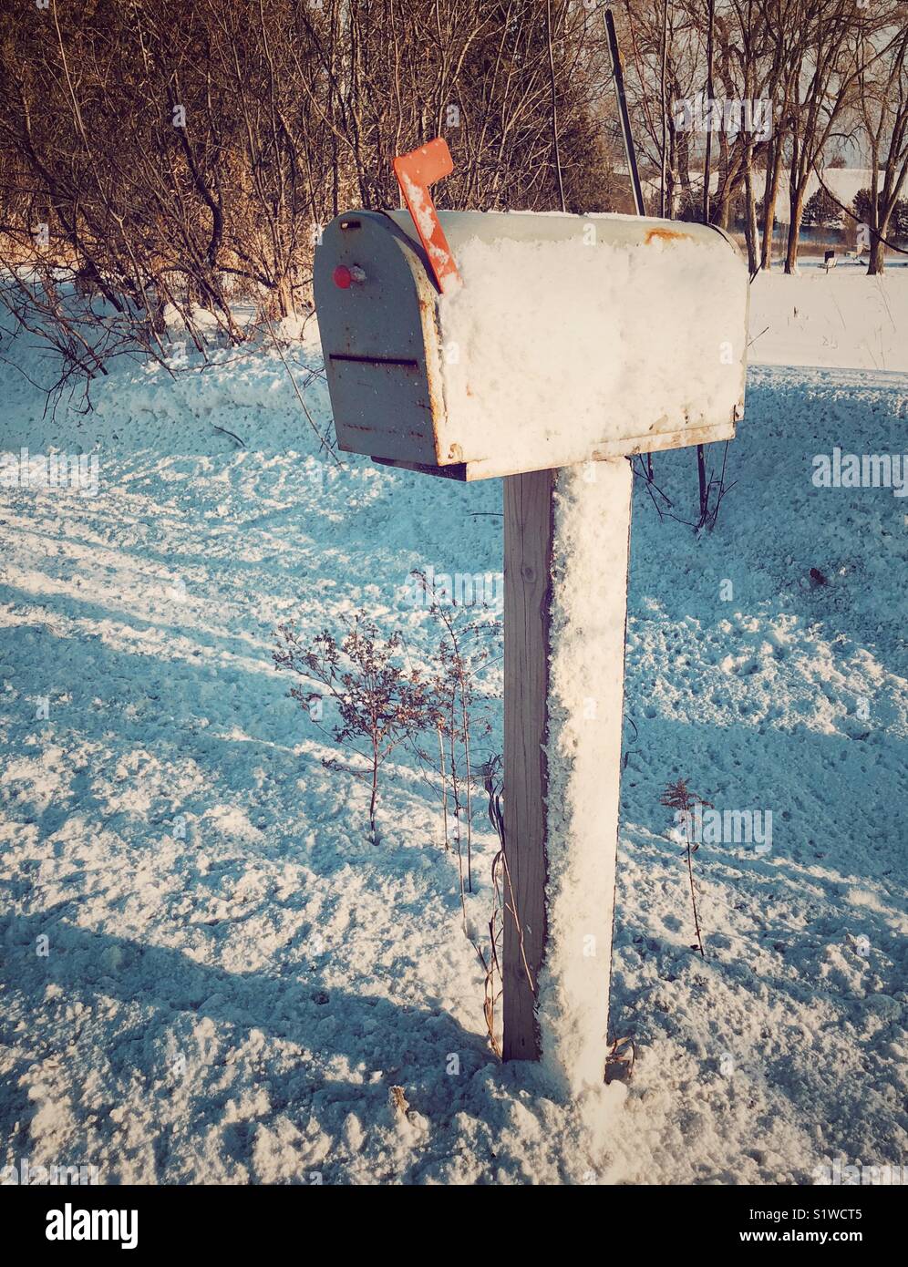 Mailbox on wooden post with red flag up covered with snow on one side