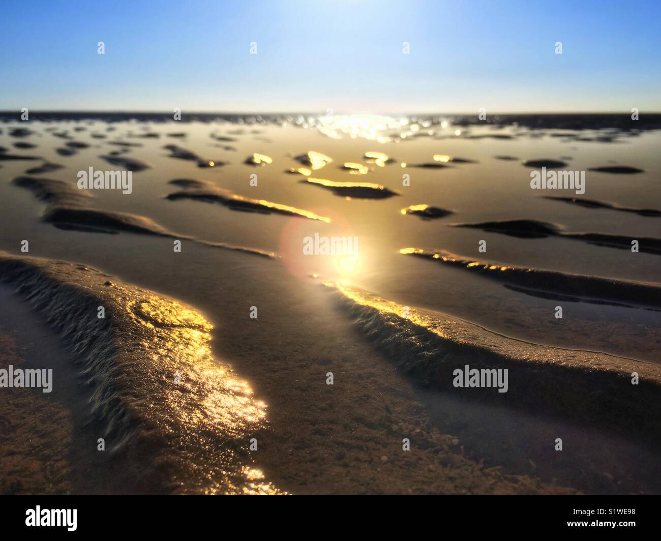 Ripples of sand on the the beach at low tide with the sun reflecting in the water - Smartphone Captured Stock Image