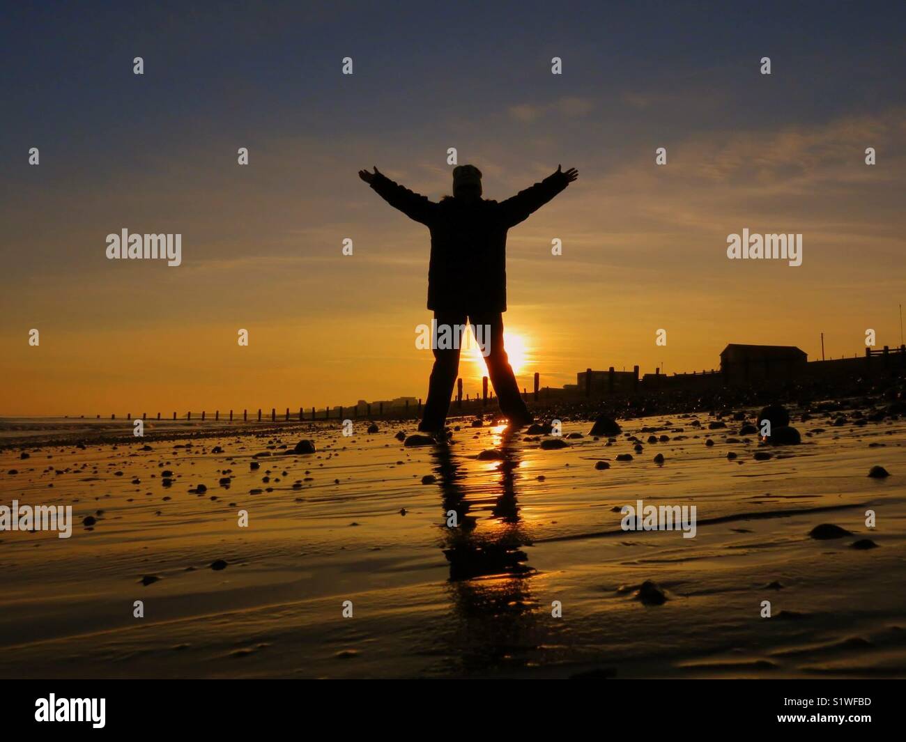 Lady with arms outstretched on the beach at sunset - Smartphone Captured Stock Image