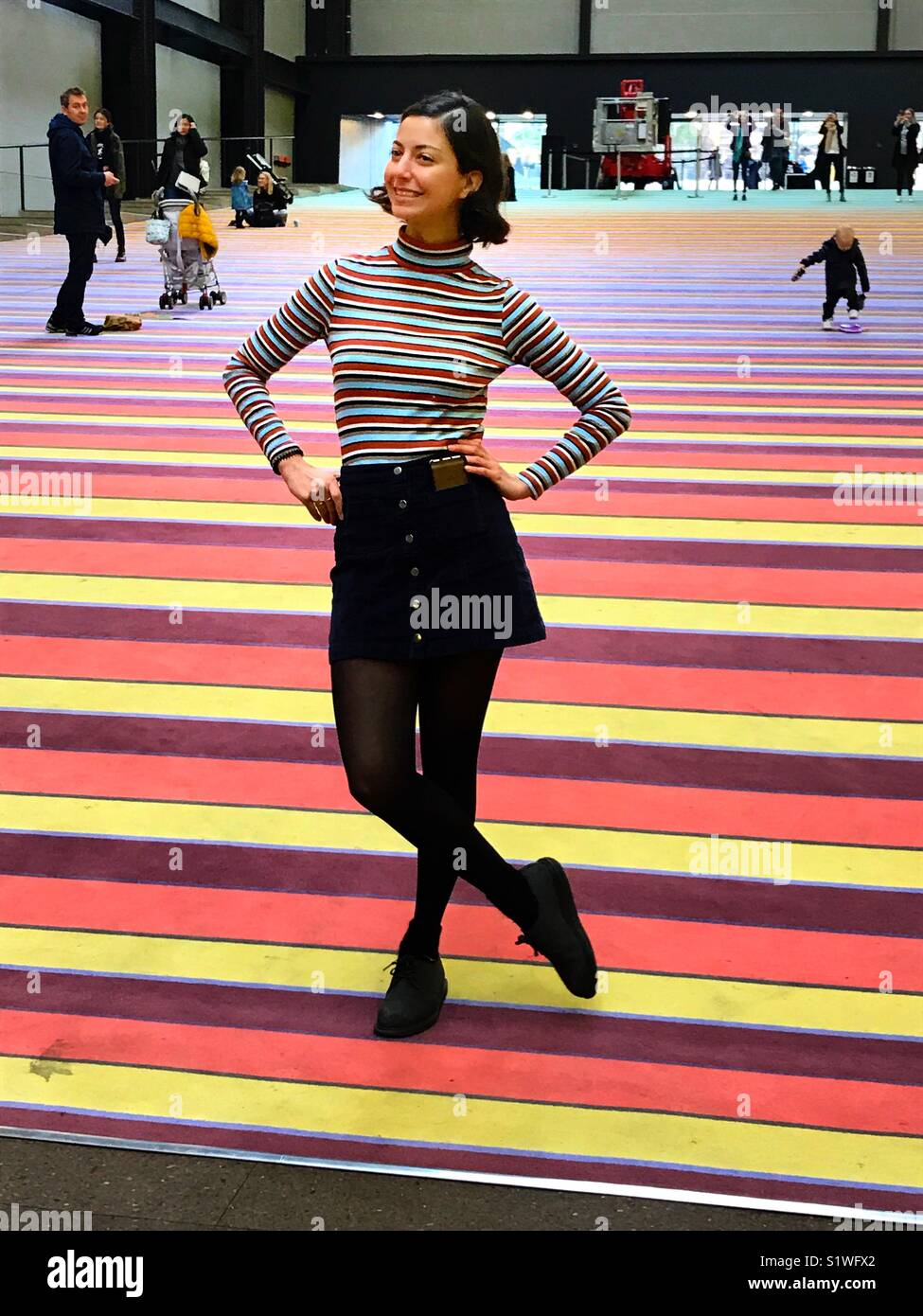 Young lady in striped jumper posing on the striped ramp in the Turbine Hall of Tate Modern Art Gallery, London Stock Photo