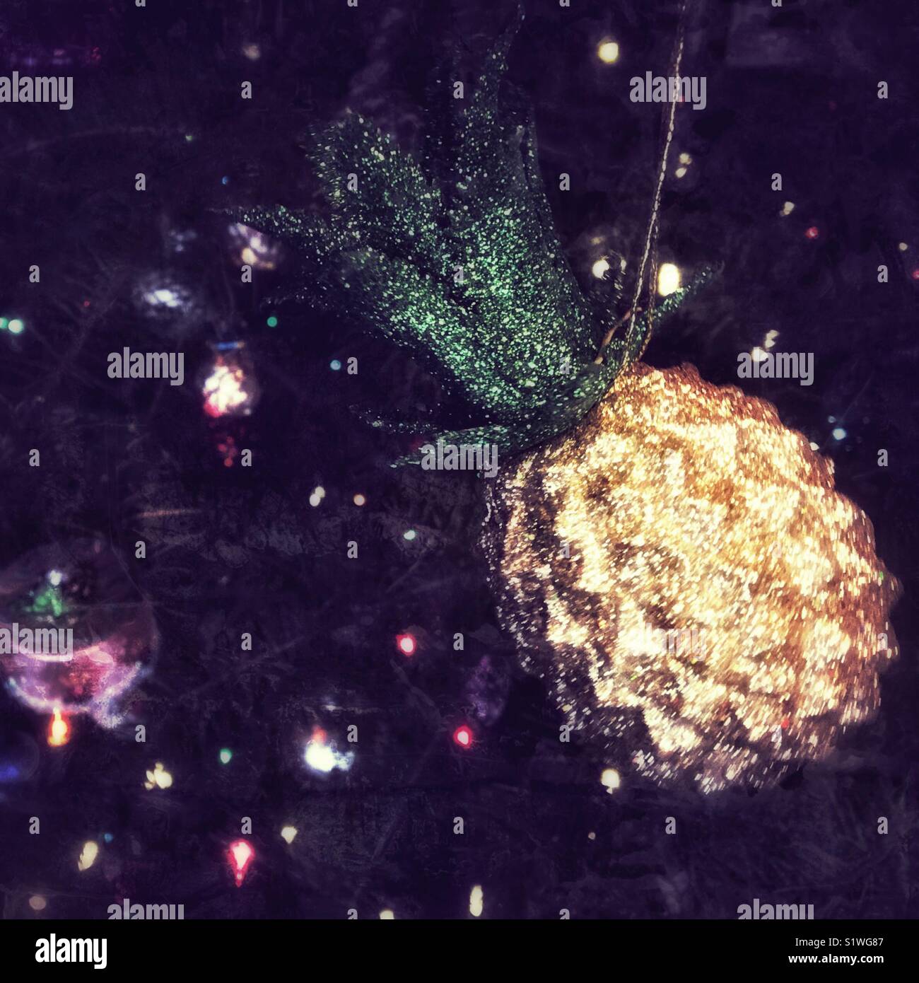 Sparkling pineapple ornament hanging on a Christmas tree. Dark edit. Square crop. Stock Photo