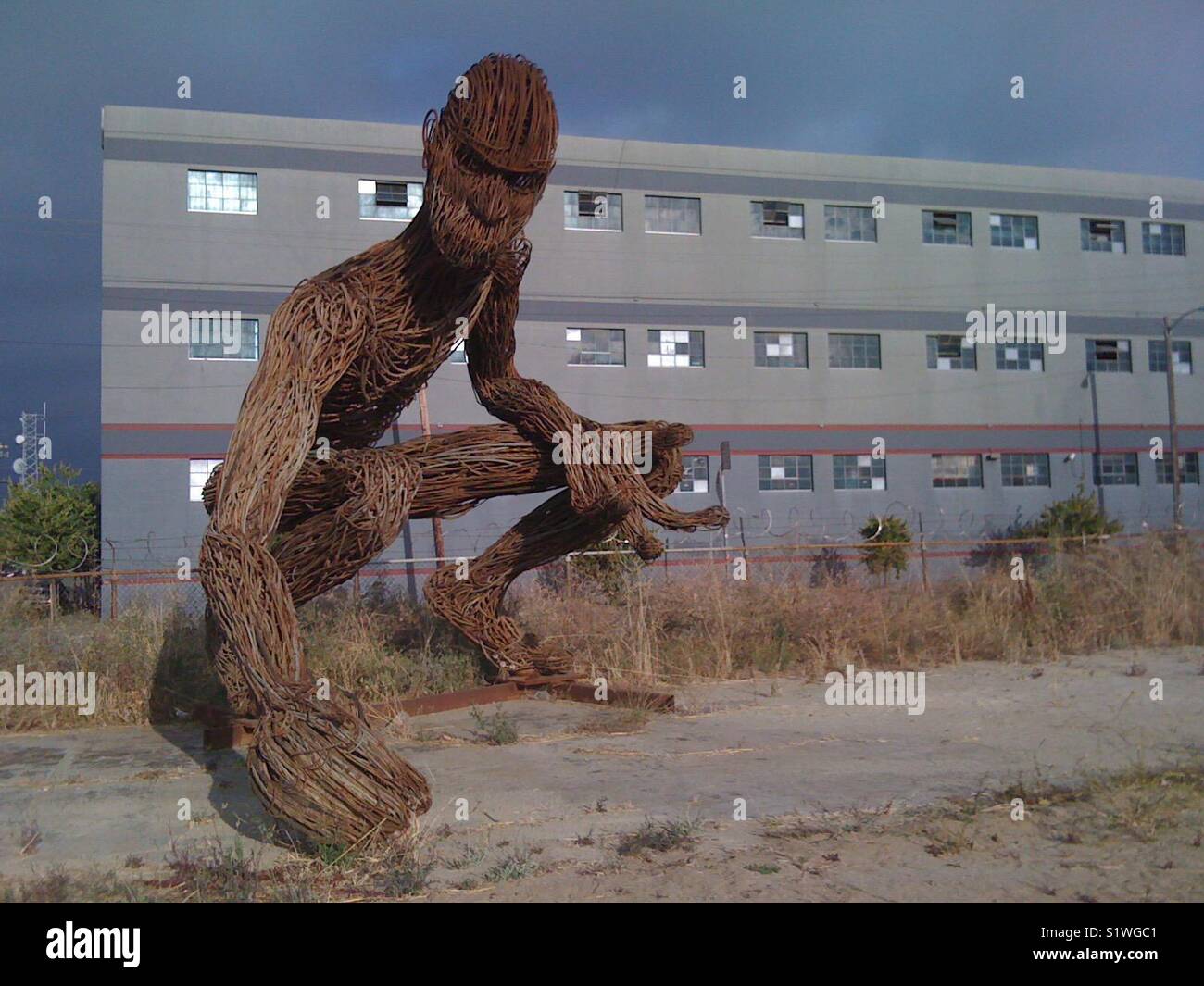 Giant steel sculpture of man kneeling with warehouse behind. West Oakland, California, USA. - Smartphone Captured Stock Image