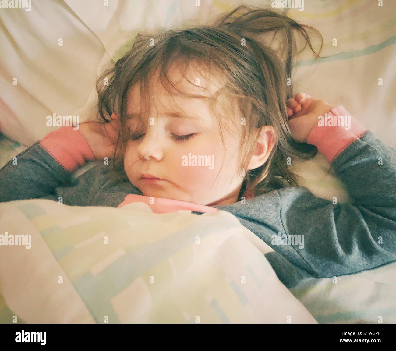 Closeup of sleeping toddler girl with messy hair and arms up in bed - Smartphone Captured Stock Image