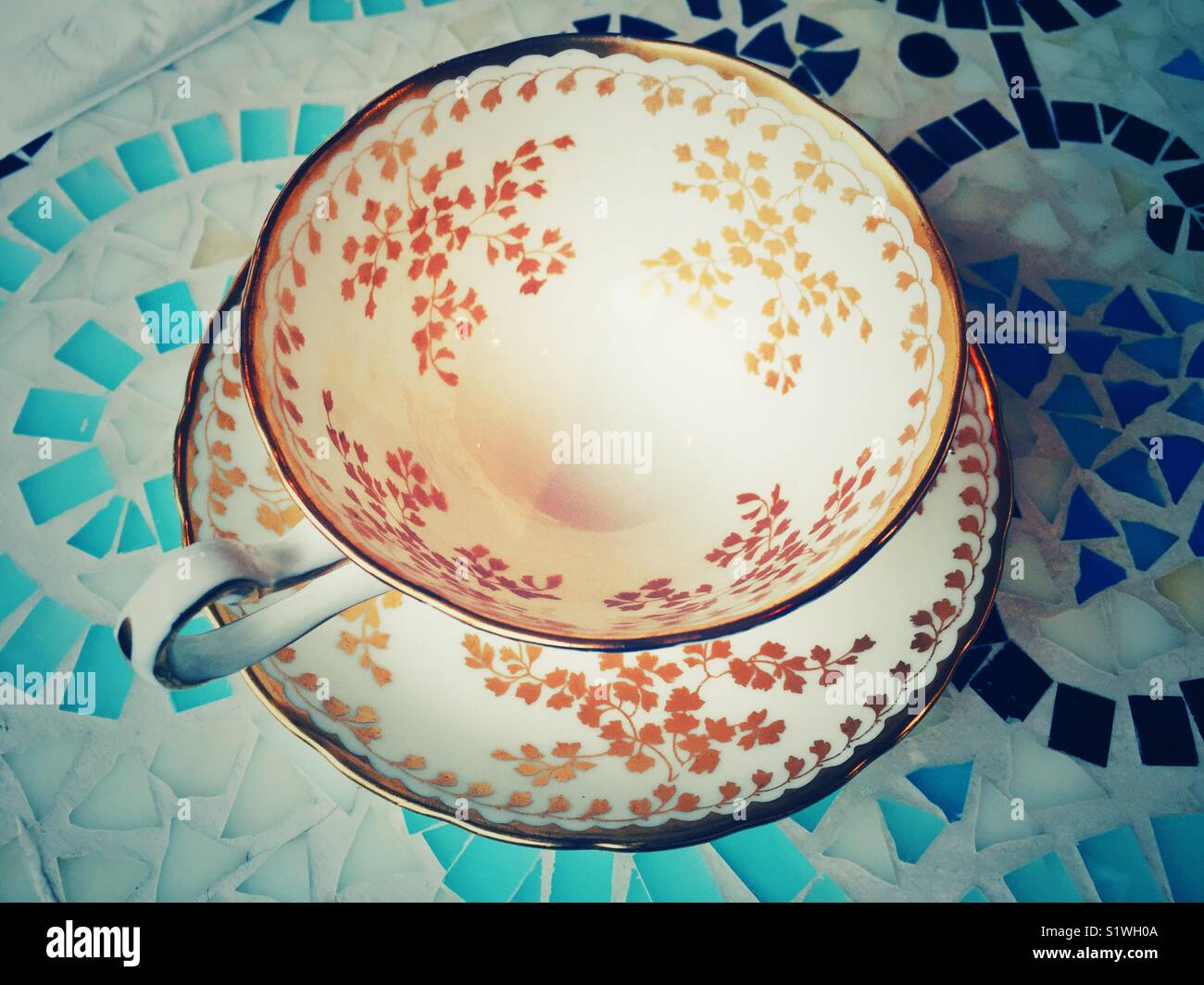 Fine porcelain empty tea cup on saucer with gilded decor on blue mosaic table - Smartphone Captured Stock Image
