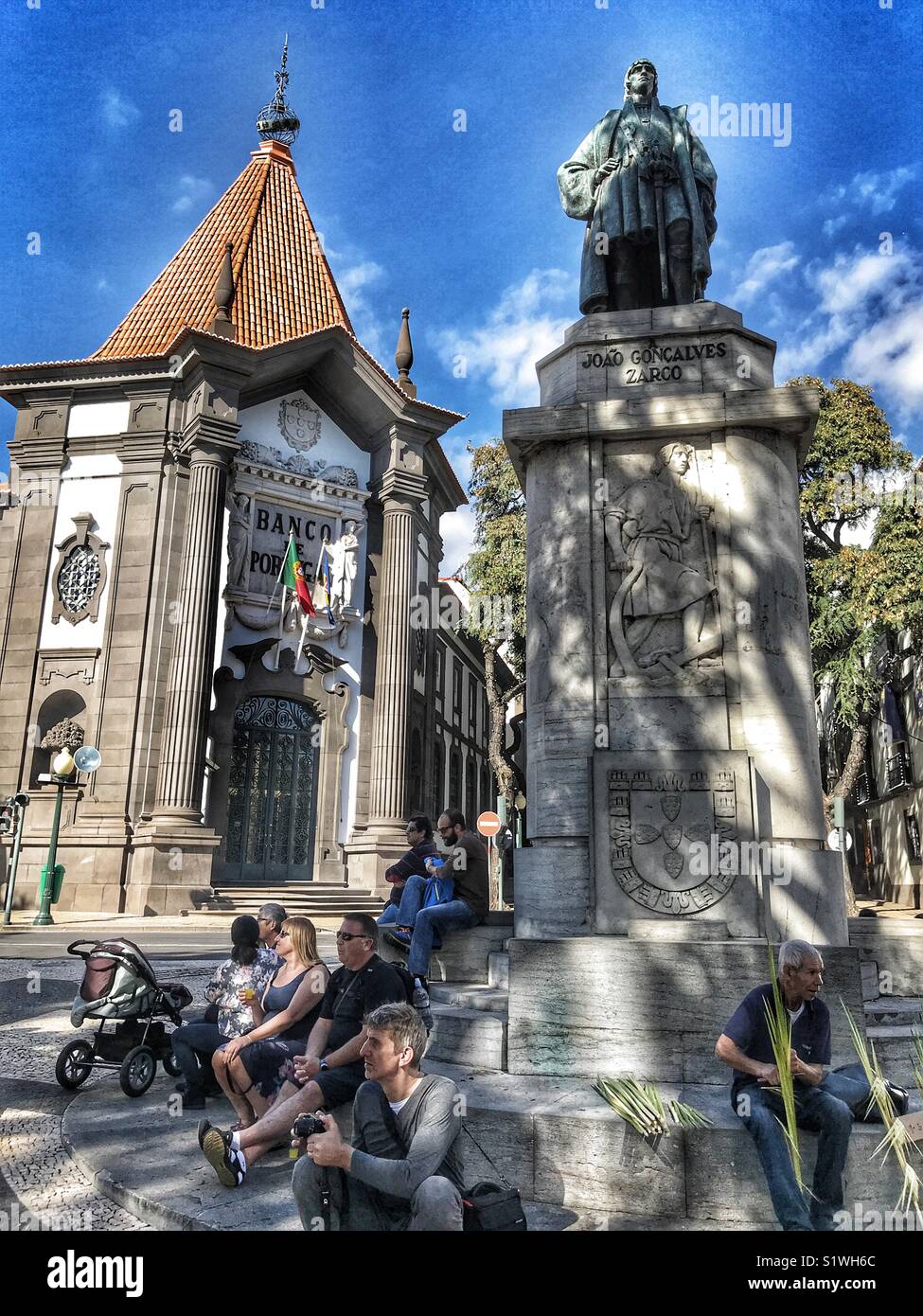 People sitting at the base of the statue of Zorca, in front of the iconic Bank of Portugal on Av. Arriaga, Funchal, Madeira, Portugal - Smartphone Captured Stock Image