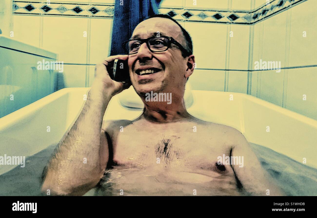 Happy middle aged man on smartphone in the bath Stock Photo