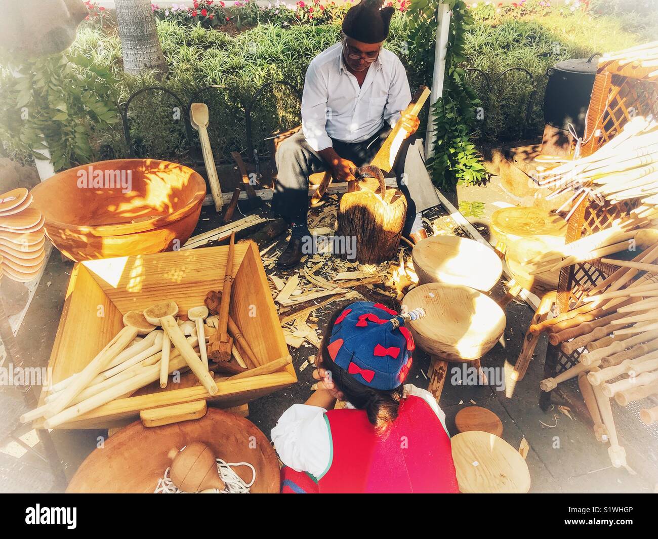 Child watching a wood carver demonstrating his craft at the Christmas Market, Funchal, Madeira, Portugal - Smartphone Captured Stock Image