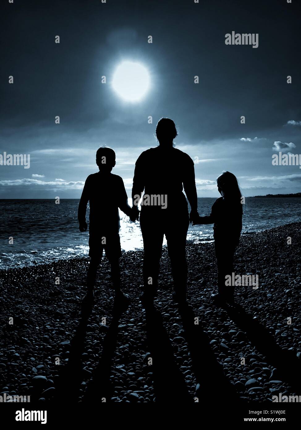 The silhouettes of 3 people - a Mother holds the hands of her 2 children as they all look forward towards a bright light. An image that illustrates social issues and has multiple uses. © COLIN HOSKINS - Smartphone Captured Stock Image