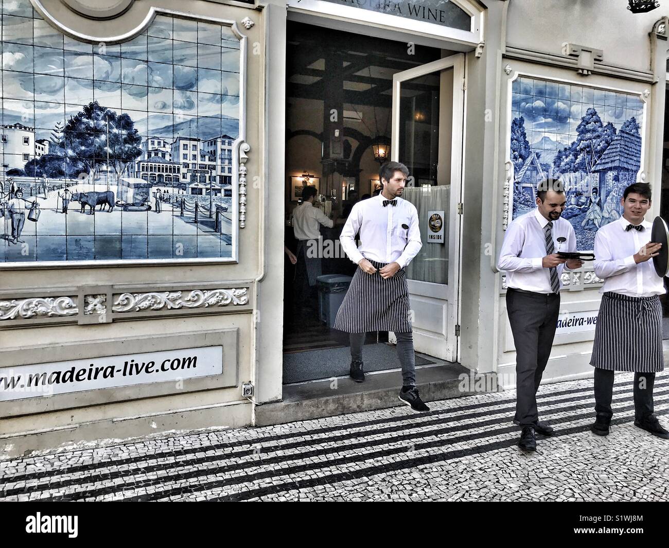 Waiters in the doorway, plus blue and white handmade glazed tiled pictures, azulejos, decorating the facade of The Ritz Hotel, Funchal, Madeira, Portugal Stock Photo