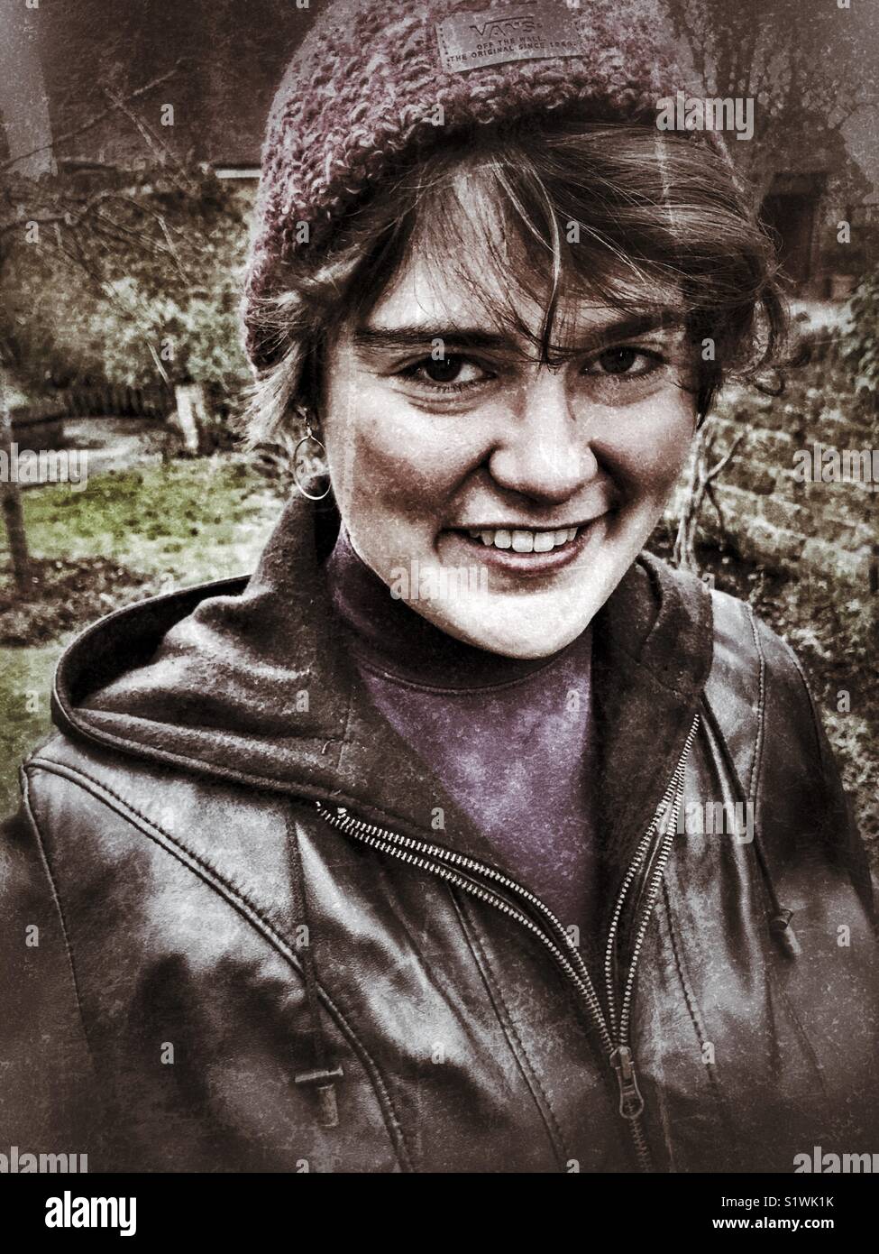 Young woman wearing a brown leather jacket and woolly hat, H&S portrait outdoors. - Smartphone Captured Stock Image