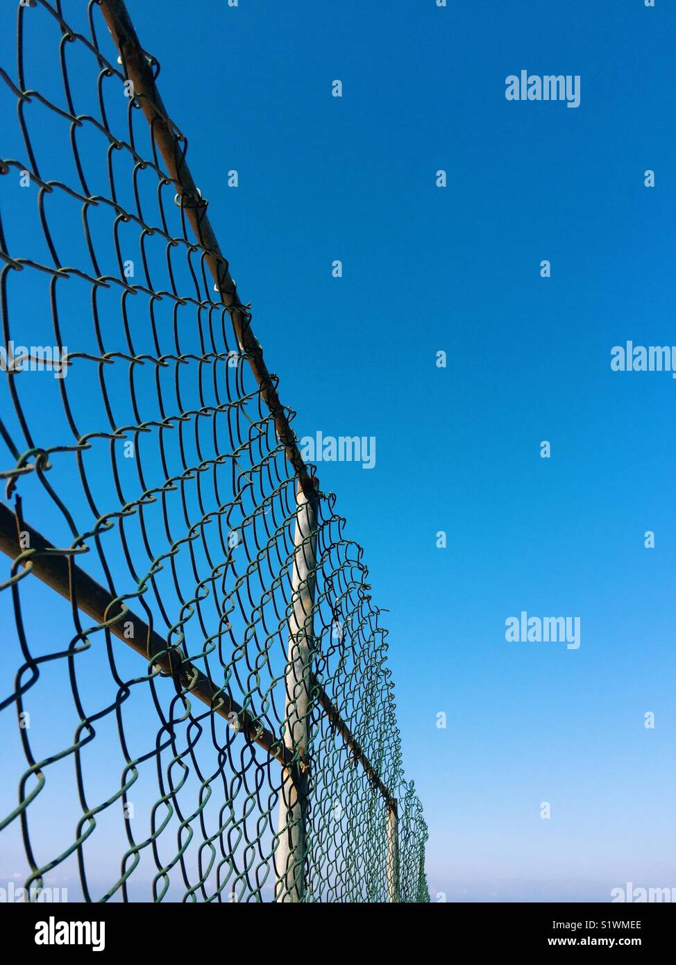 Metal chicken wire fence against blue sky Stock Photo
