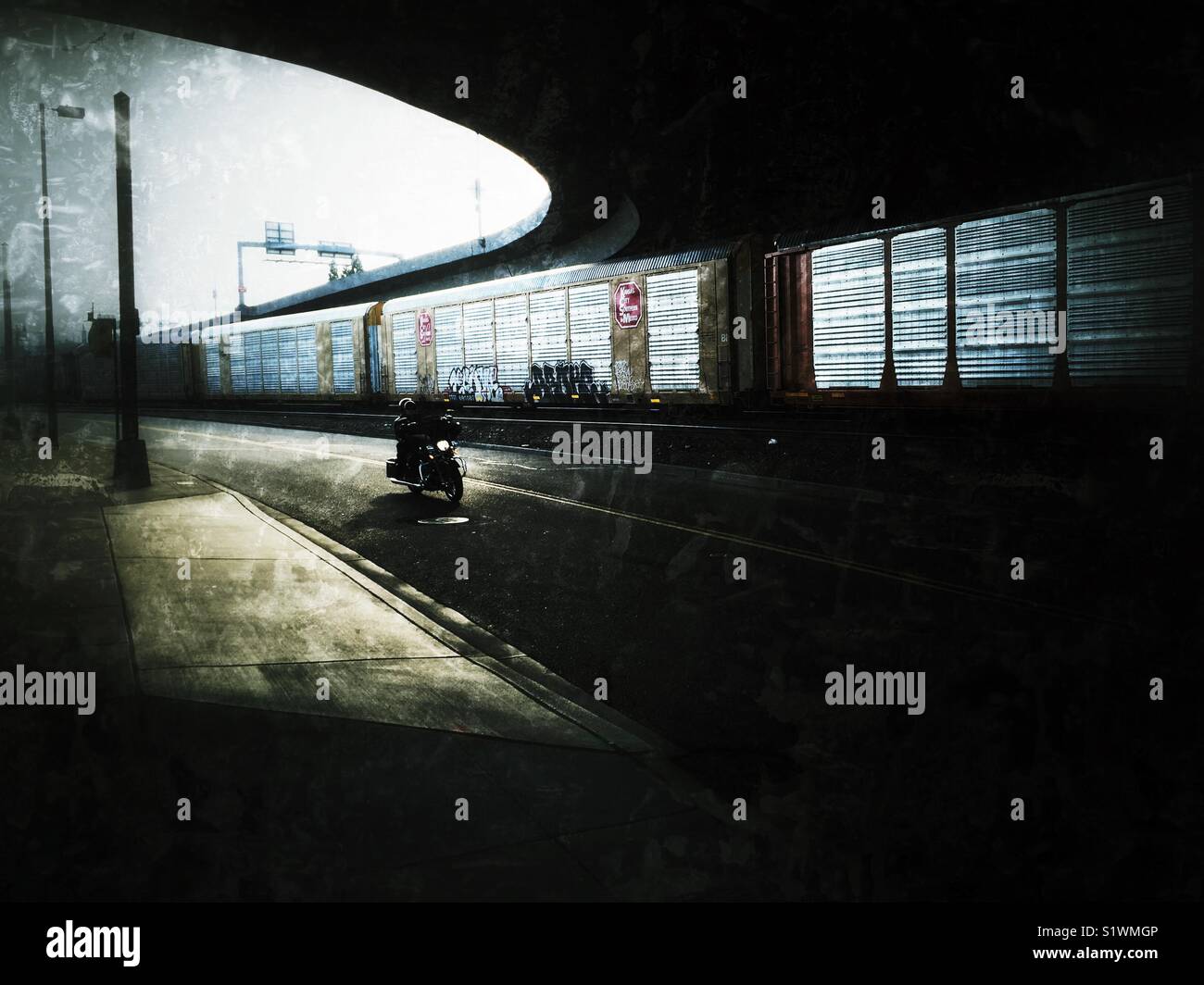 Motorcyclist riding underpass next to the freight train in Tacoma, Washington state - Smartphone Captured Stock Image