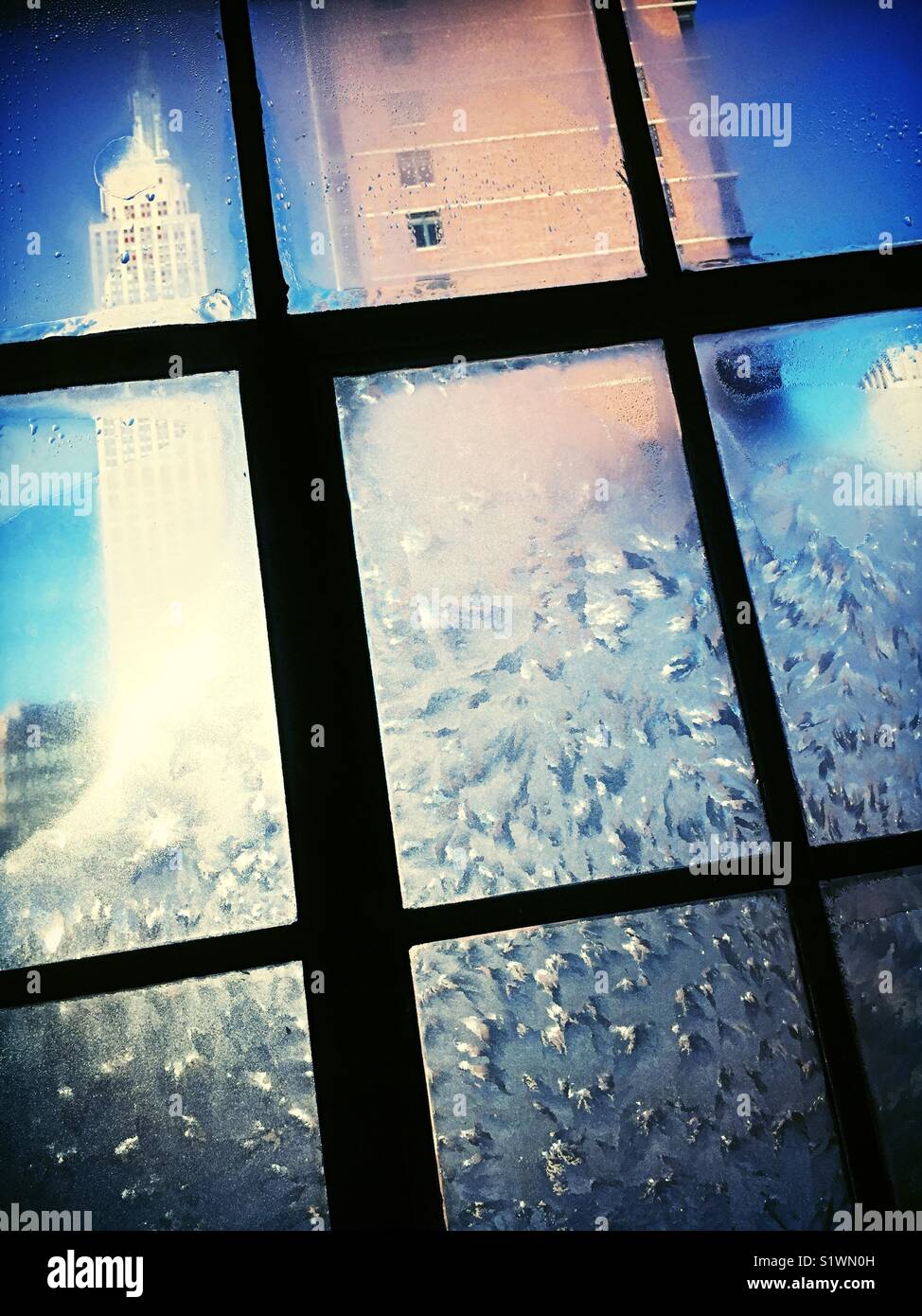View of the Empire State building through glass casement window encrusted with ice during winter storm, NYC, USA - Smartphone Captured Stock Image