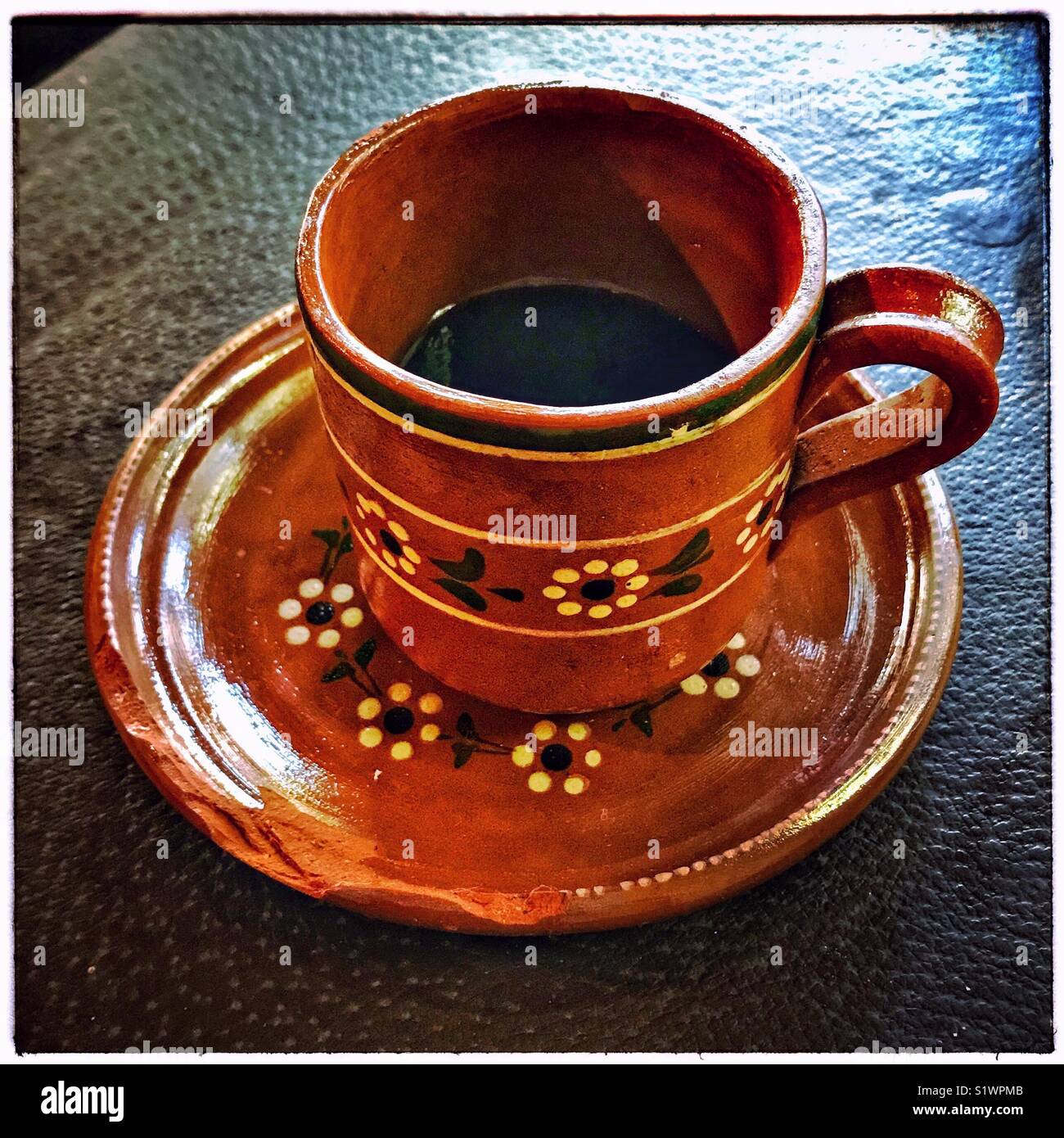 https://c8.alamy.com/comp/S1WPMB/a-mexican-clay-cup-and-chipped-saucer-with-a-flower-design-is-partially-S1WPMB.jpg