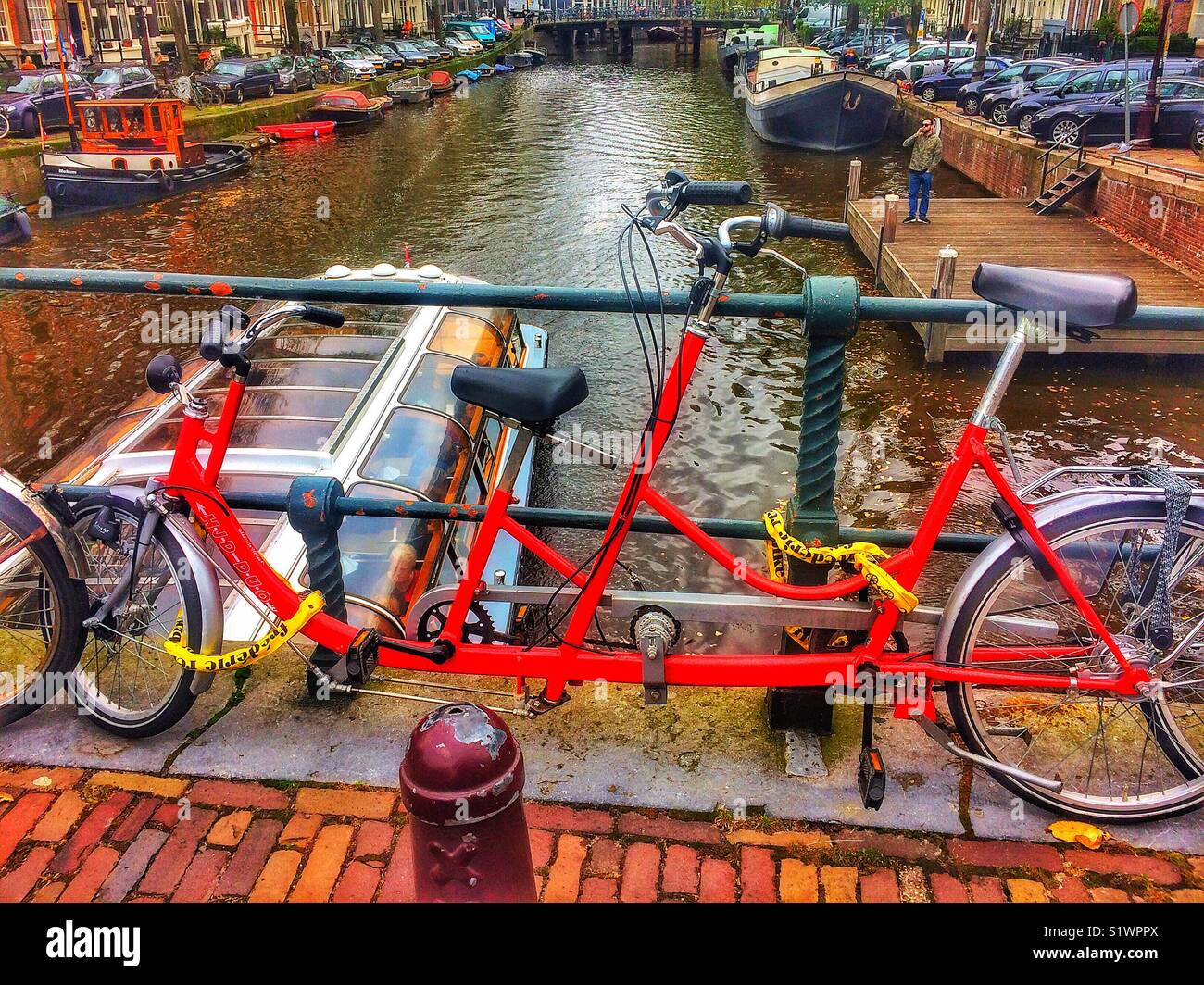 Tandem bicycle chained to railings above canal, Amsterdam, Netherlands - Smartphone Captured Stock Image
