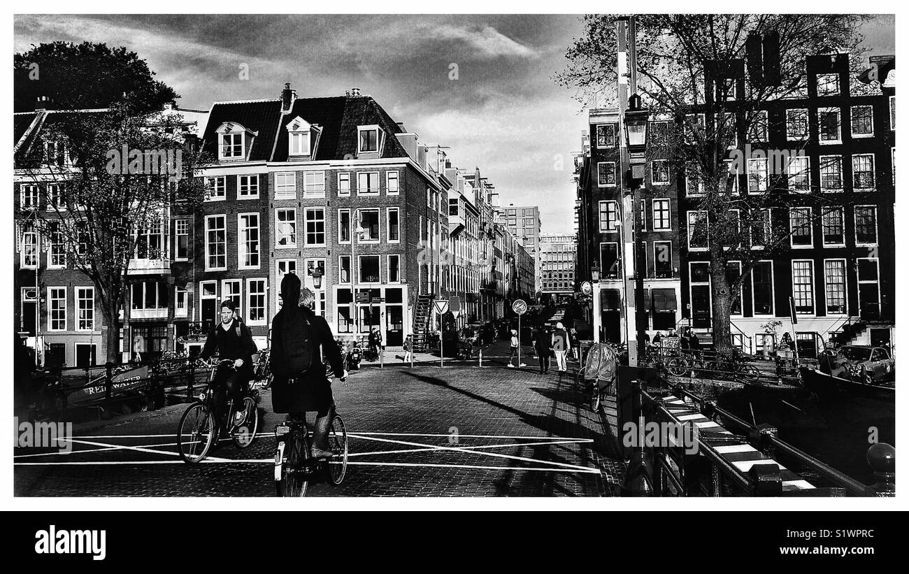 Cyclists on the Magere (Skinny Bridge) over the Amstel River leading into Nieuwe Kerkstraat, Amsterdam, Netherlands Stock Photo