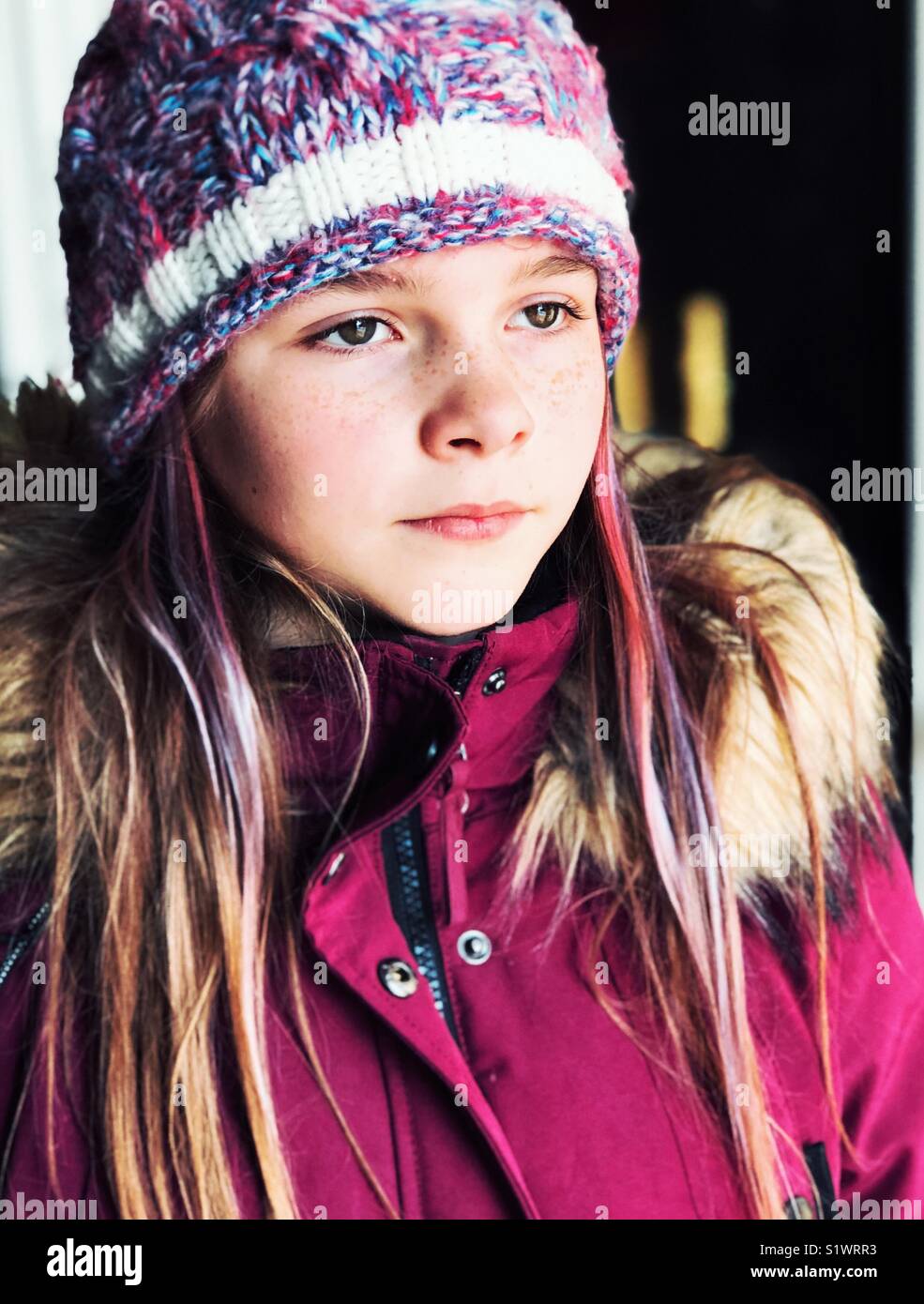 Portrait of 10 year old girl with purple hair streaks wearing winter coat and knit hat looking to the side Stock Photo