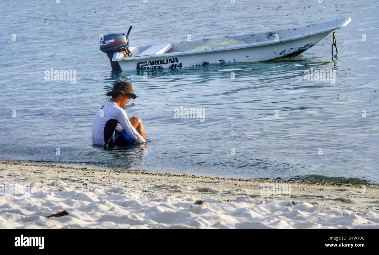 Man sitting in the water after fishing. His small boat anchored beside him - Smartphone Captured Stock Image