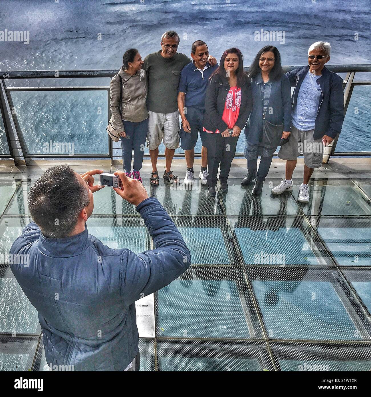 Man taking a photo of group of people standing on the glass skywalk  viewing platform 580m above the sea, Miradouro do Cabo Girao, Madeira, Portugal - Smartphone Captured Stock Image