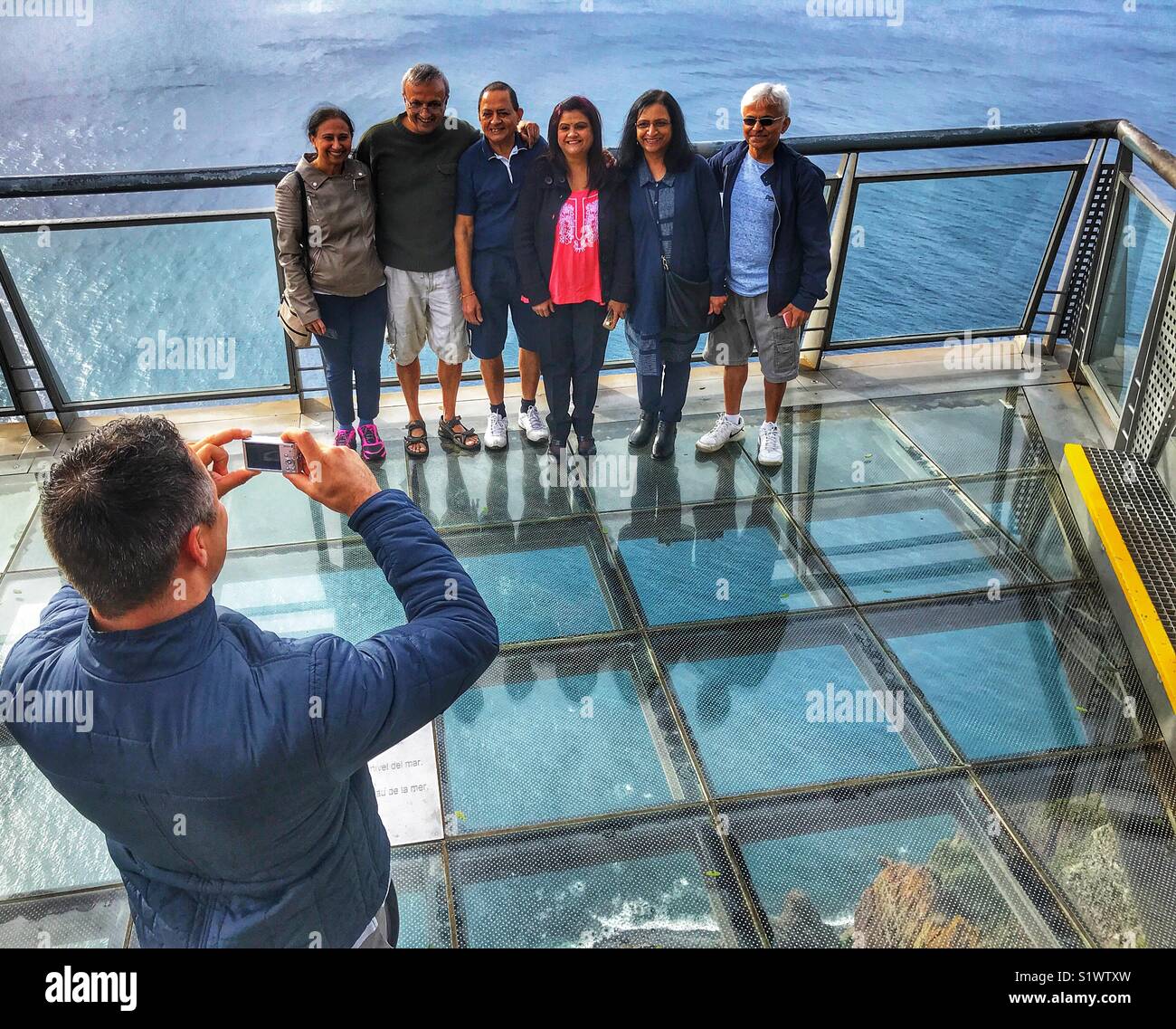 Man taking a photo of group of people standing on the glass skywalk  viewing platform 580m above the sea, Miradouro do Cabo Girao, Madeira, Portugal - Smartphone Captured Stock Image