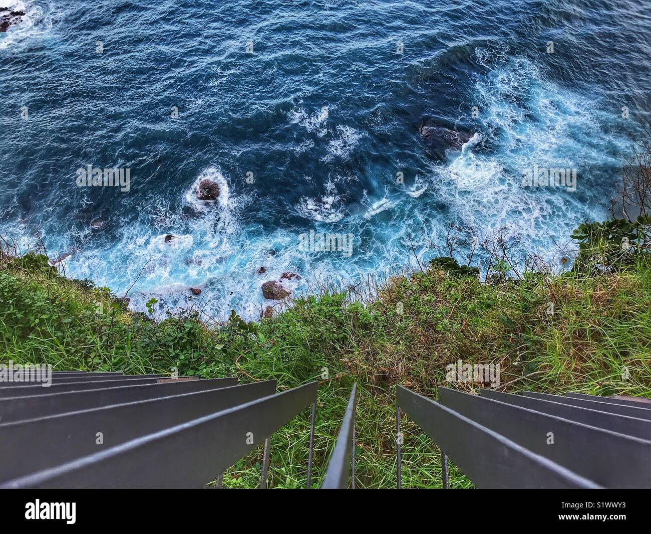 Looking over iron railings down a cliff to rough sea, waves and rocks below, Madeira, Portugal - Smartphone Captured Stock Image