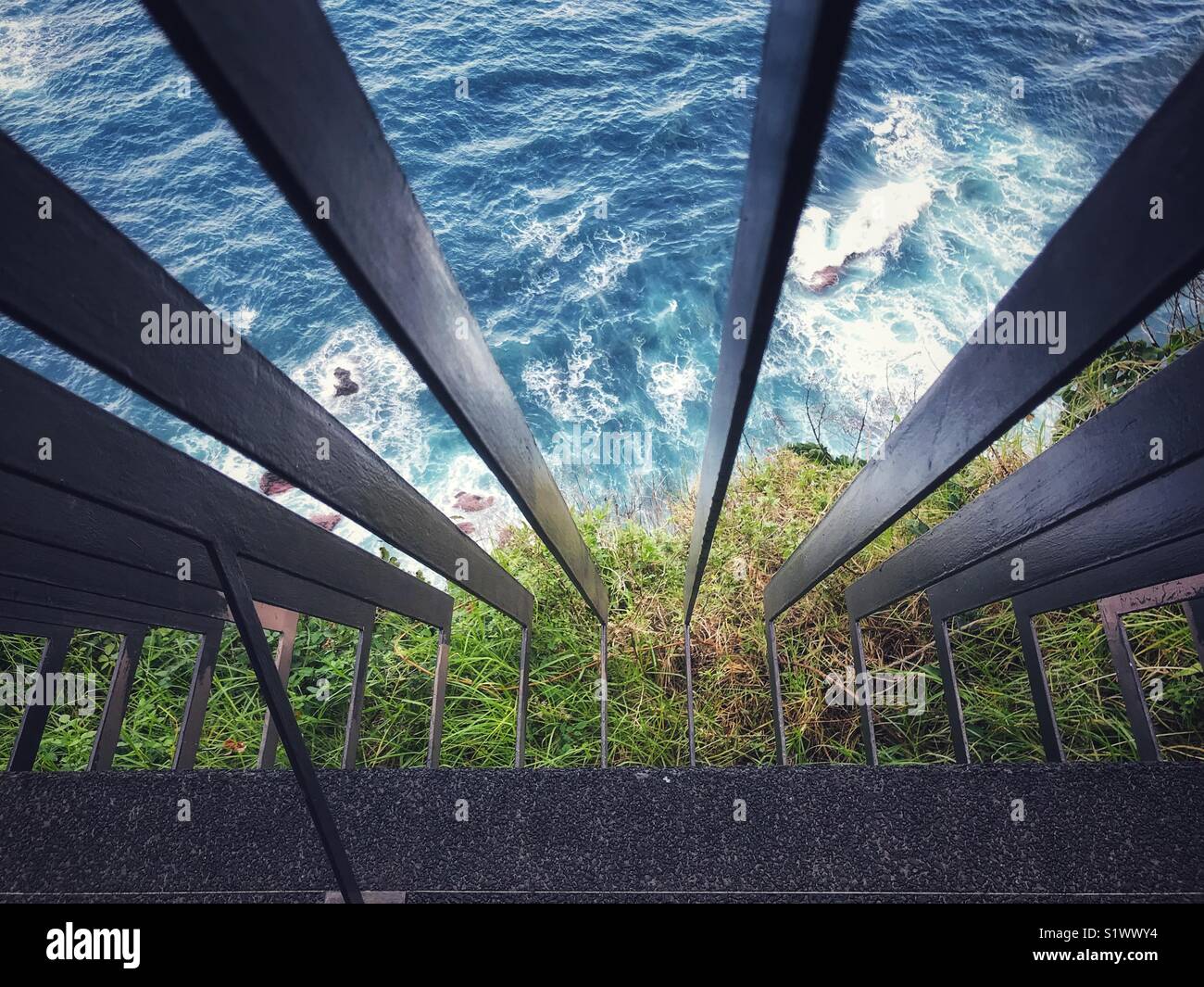 Looking over iron railings down a cliff to rough sea, waves and rocks below, Madeira, Portugal - Smartphone Captured Stock Image