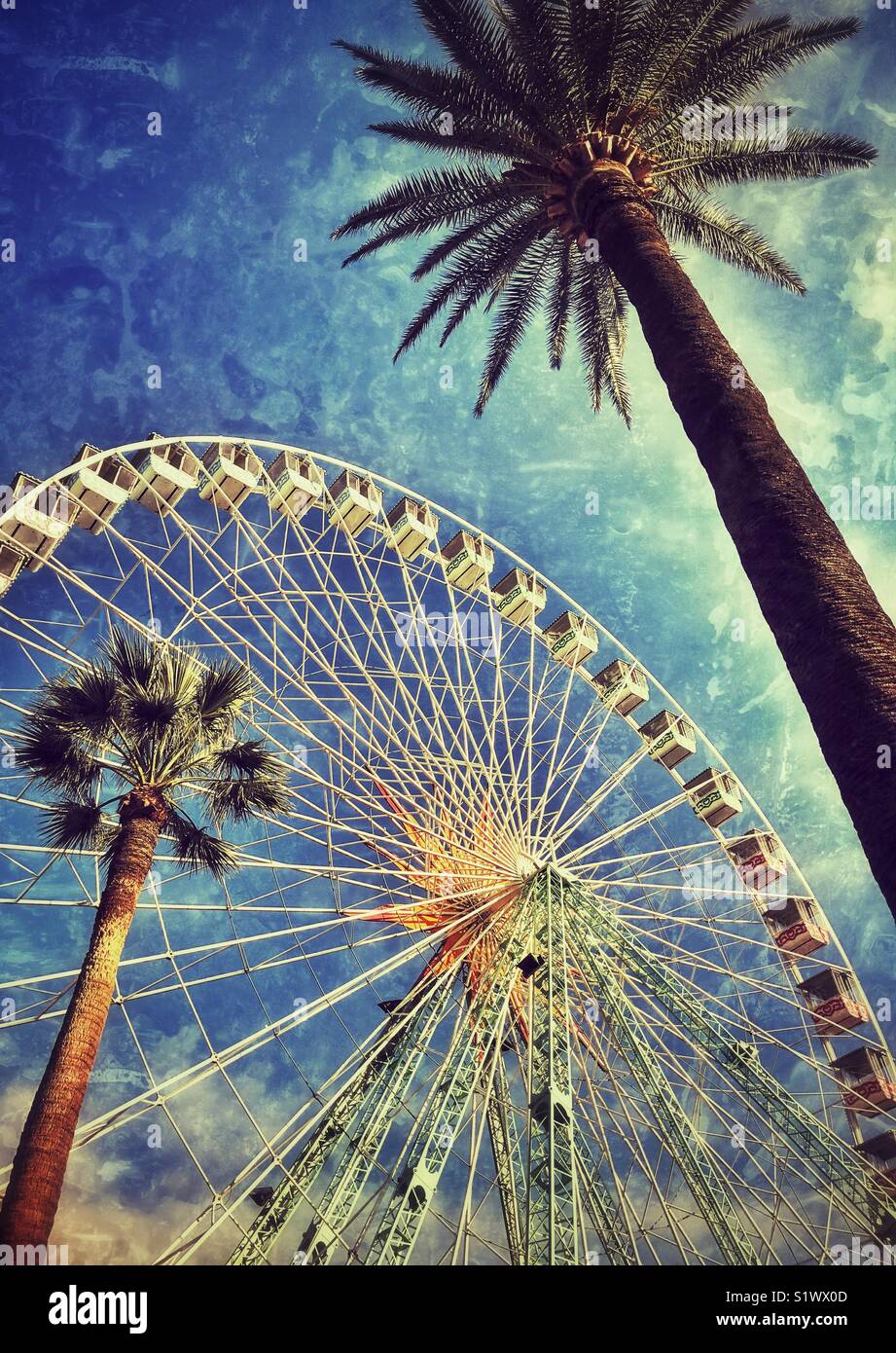 A colour grunge effect image of the large Ferris Wheel in the Place Massena & Albert 1st Garden’s area of Nice, Còte a’Azure, France. The view is complimented by two palm trees. Photo © COLIN HOSKINS. - Smartphone Captured Stock Image