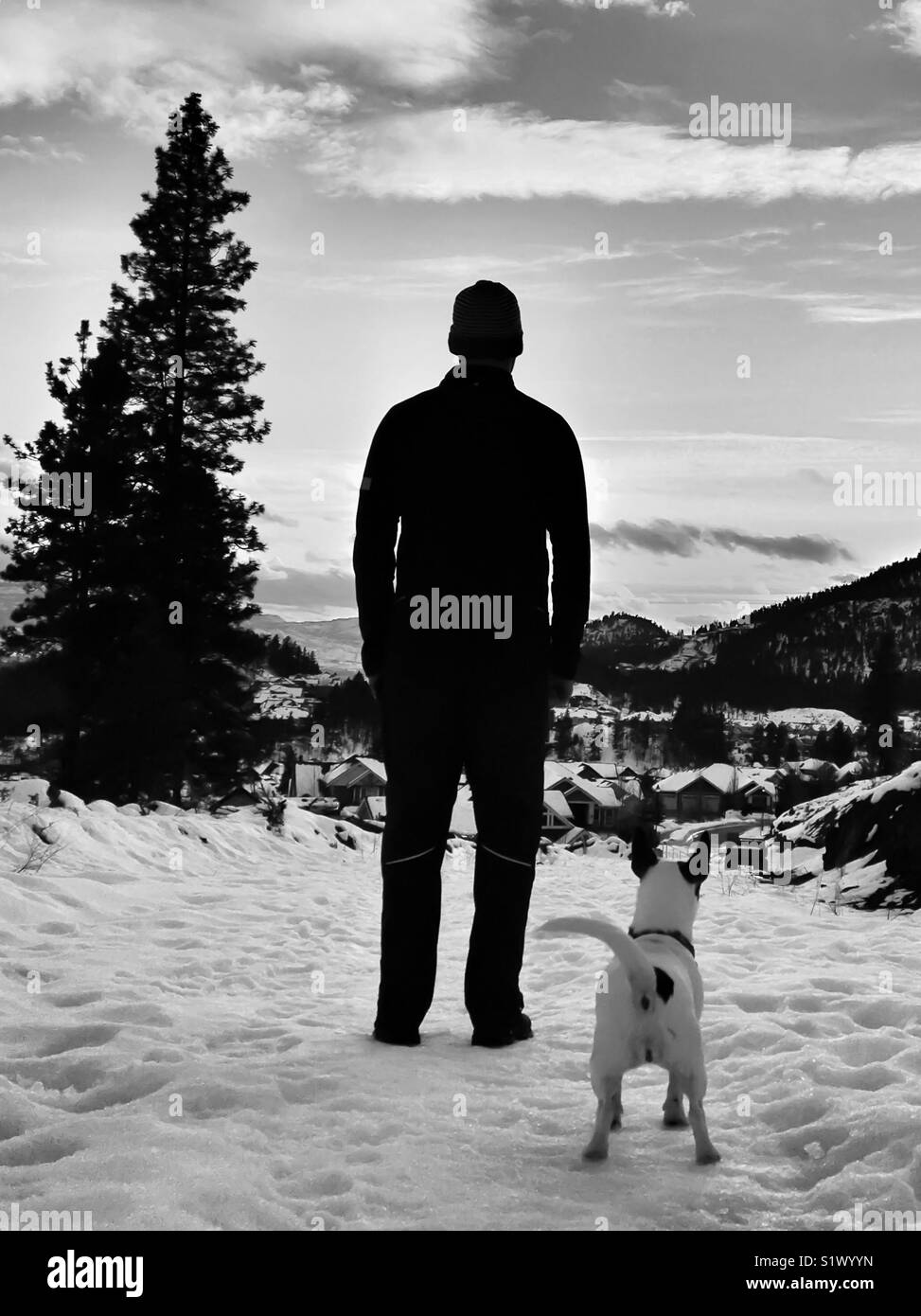 Silhouette of a man standing in the snow with dog. In black and white. Stock Photo