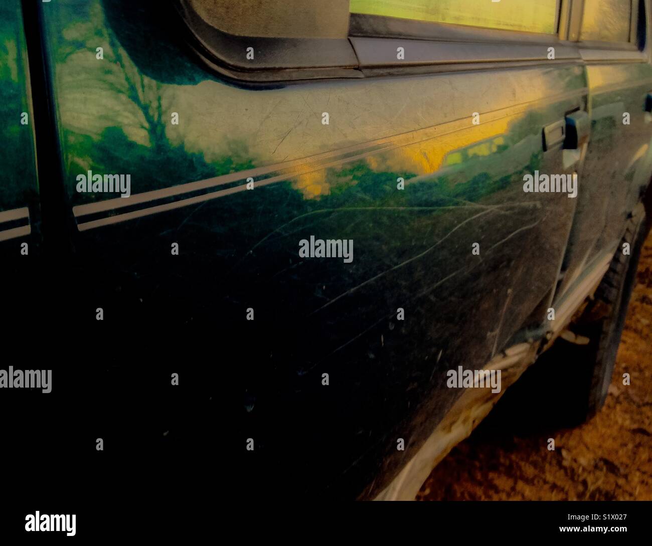 Green vehicle door with dent and reflection of sunset and truck - Smartphone Captured Stock Image