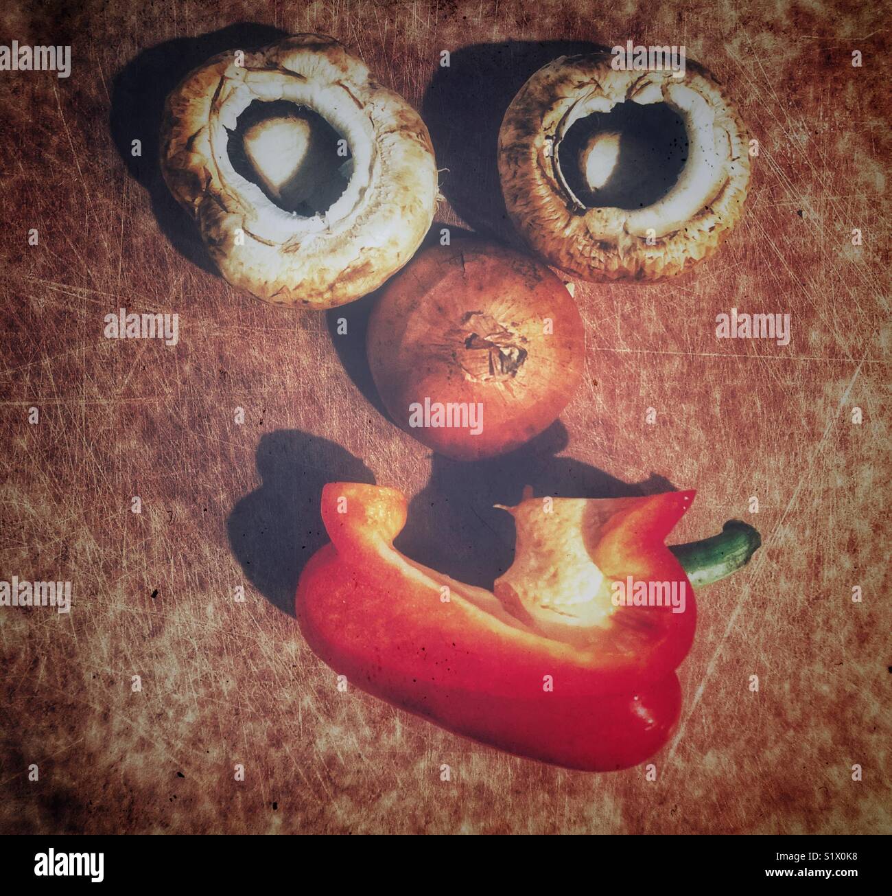 Two large white mushroom caps, half a yellow onion and piece of red sweet bell pepper arranged on a cutting board to look like a happy face - Smartphone Captured Stock Image