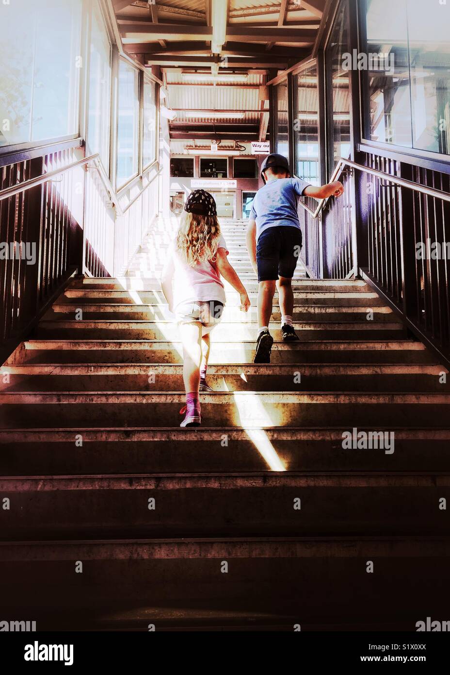 Two kids climb stairs at railway station. Young boy and girl walk up stairway through sunbeam - Kiama, NSW, Australia Stock Photo